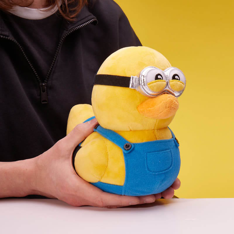 Sárga Minion kacsa játék, fekete szemüveggel és kék kezeslábassal, kézben.