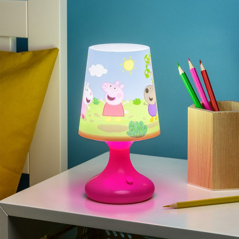 Rózsaszín Peppa malac lámpa fehér asztalon, ceruzákkal. Kék háttér.