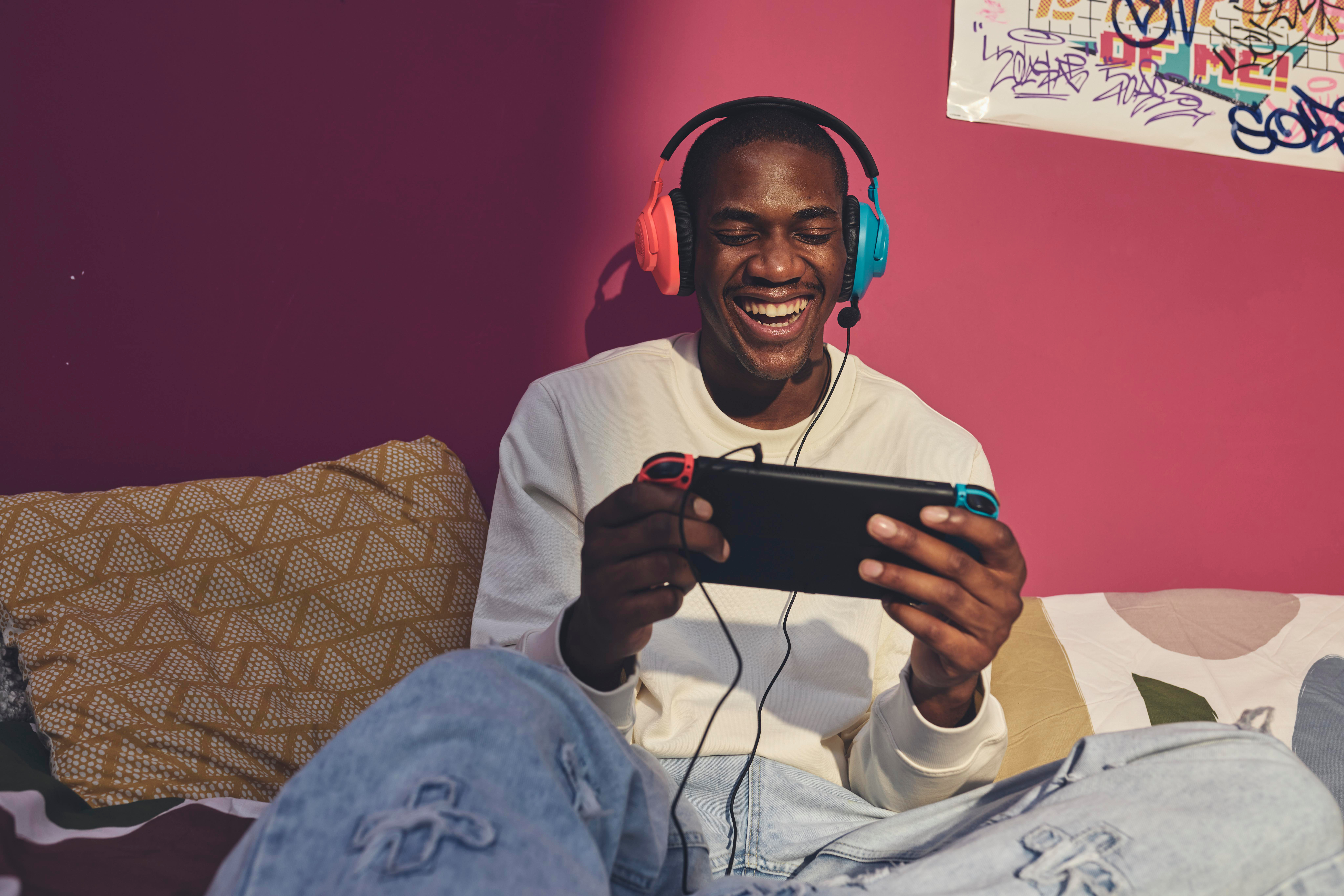 Ein glücklicher Schwarzer Mann, der Kopfhörer trägt und Switch spielt. Bunter Hintergrund.