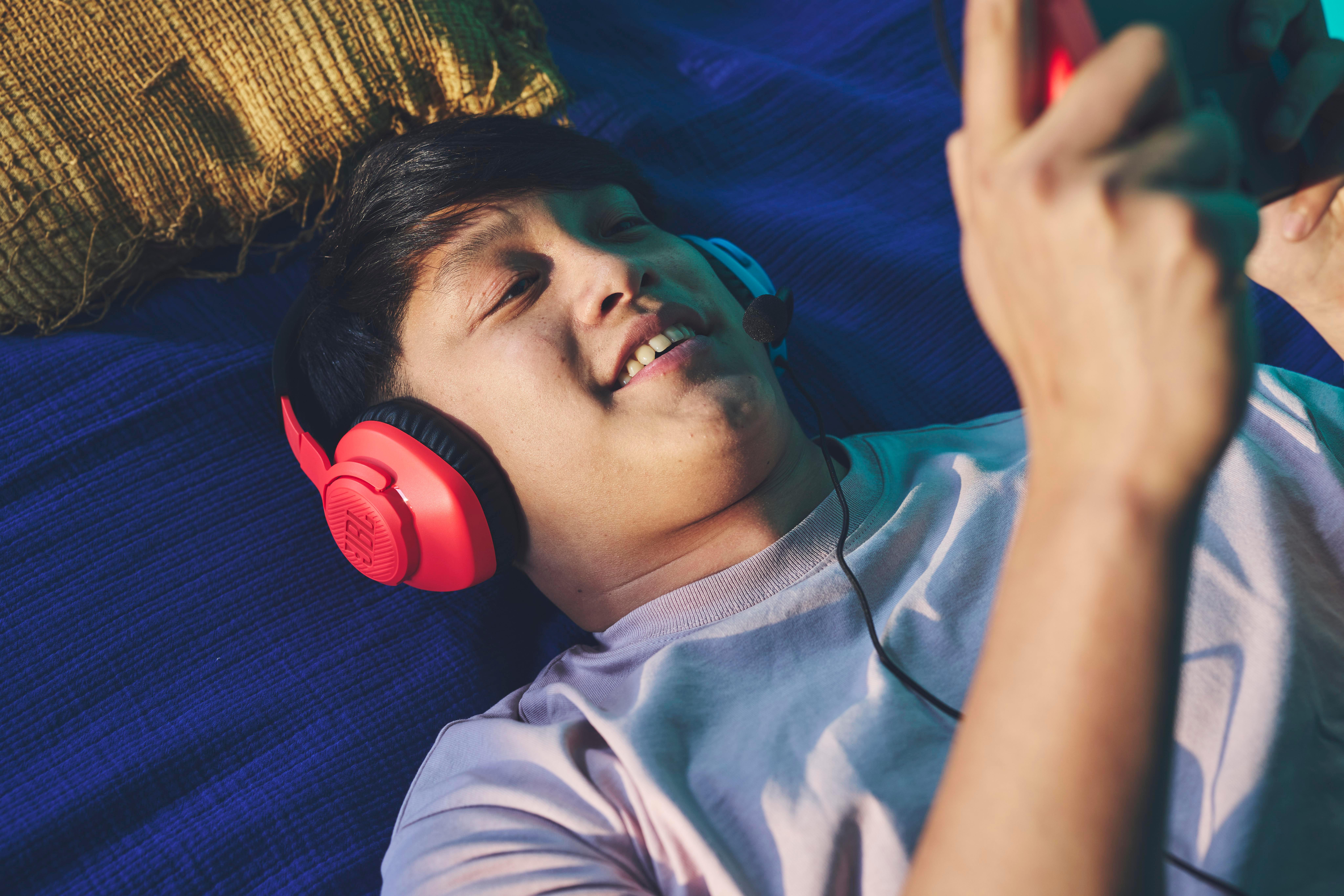 Ein Mann, der auf einer blauen Fläche liegt, trägt rote Kopfhörer und schaut auf ein Smartphone.