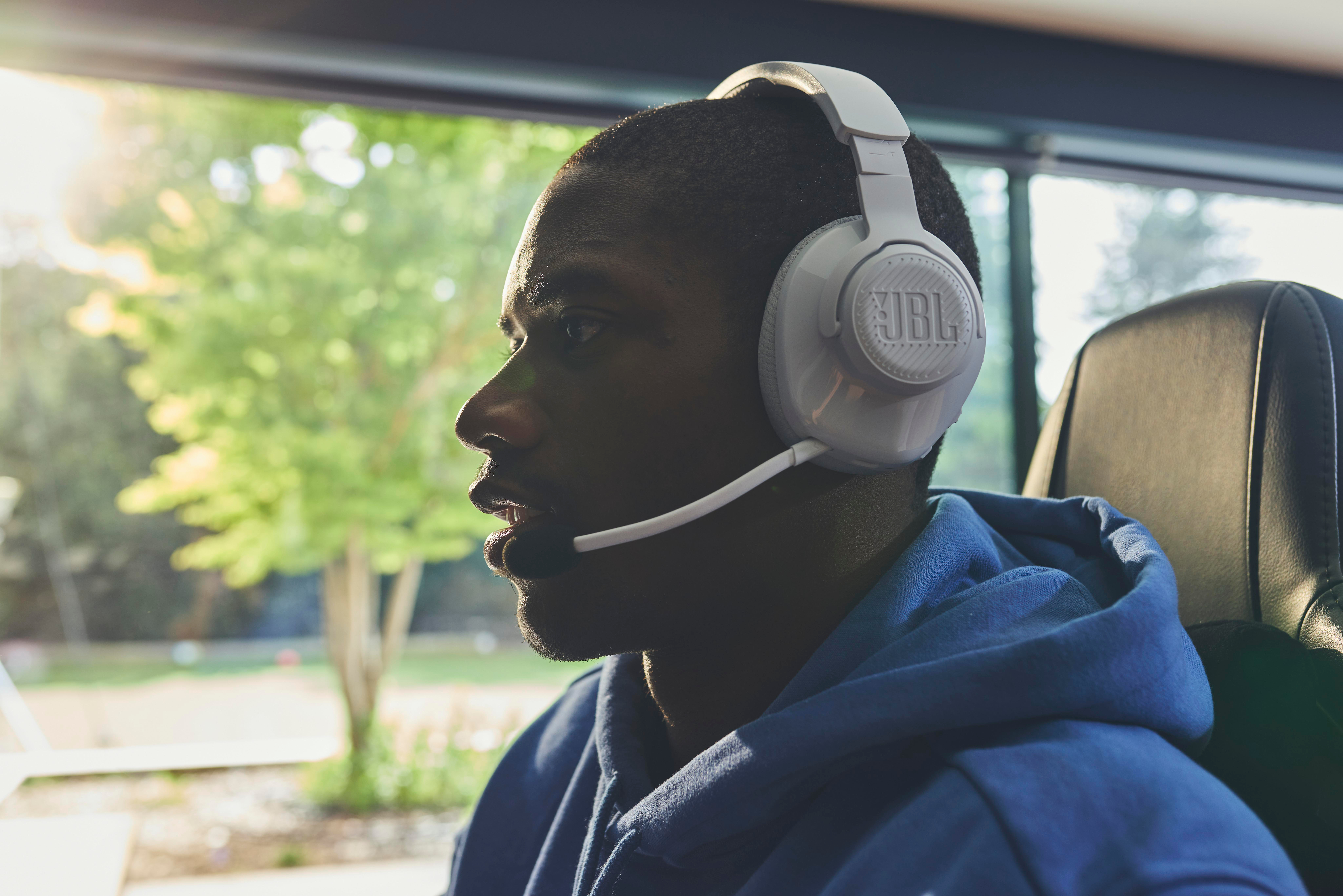 Mann mit weißem JBL-Headset mit Mikrofon. Er ist in einem Raum mit Fenster.