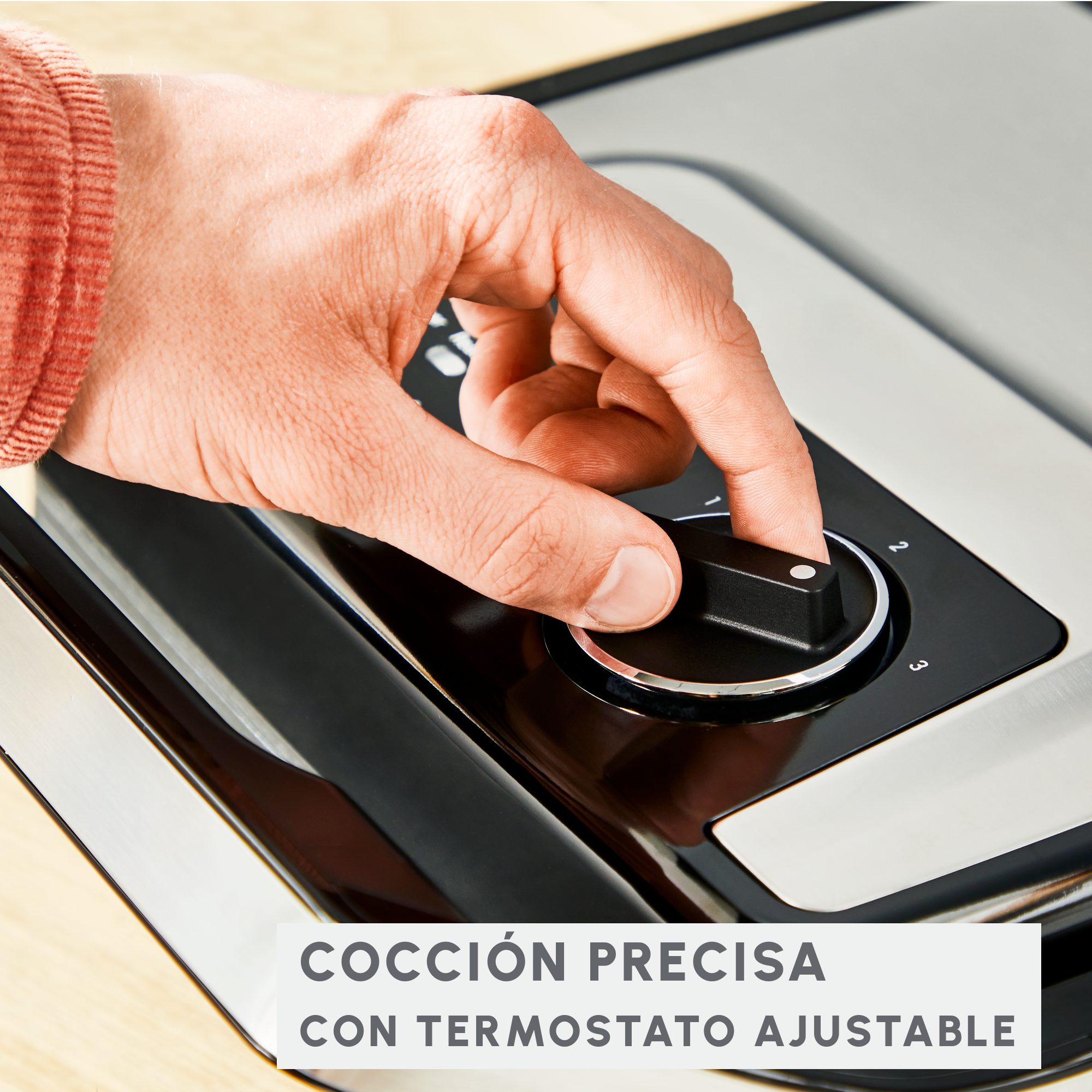 Una mano girando una perilla en un dispositivo, el texto dice: Cocción precisa con termostato ajustable.