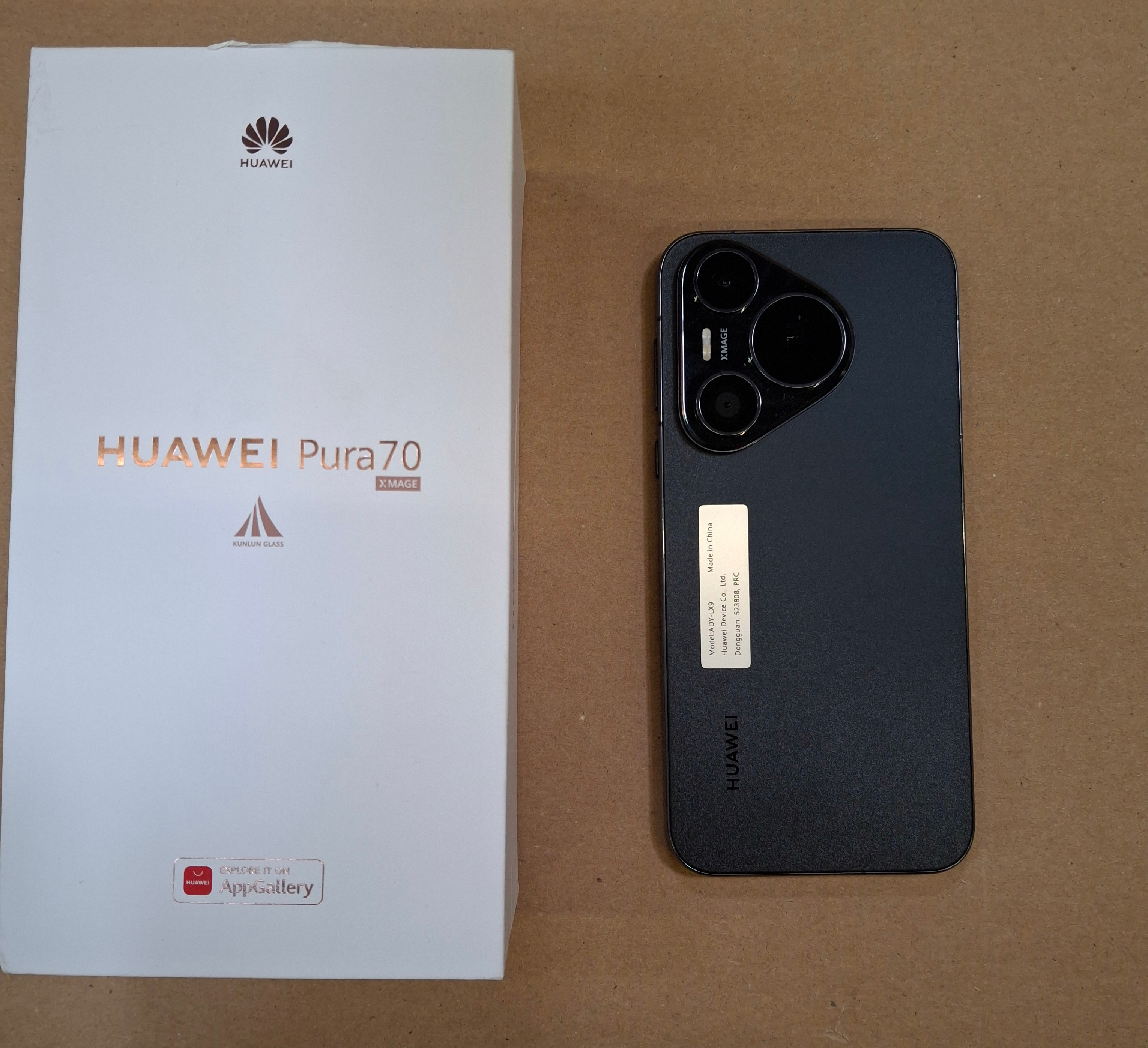 Biały telefon Huawei Pura 70 Xmage i jego pudełko na brązowej powierzchni.