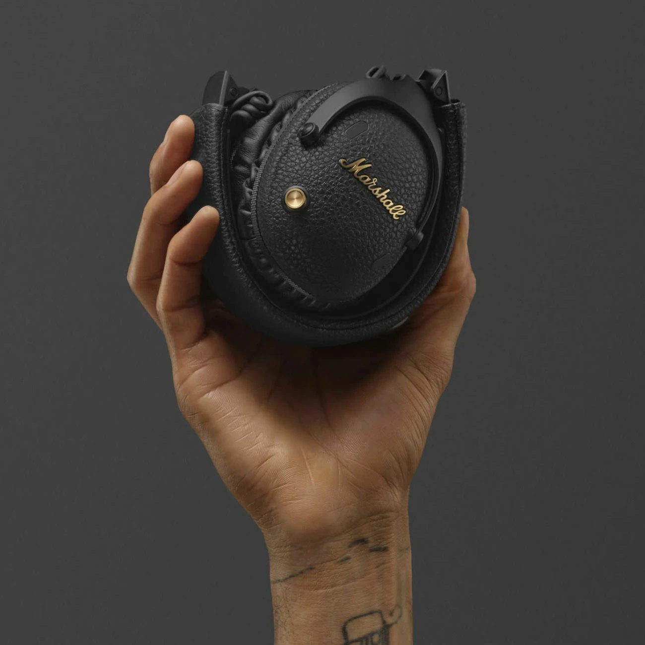 Dłoń trzymająca złożone czarne słuchawki Marshall na szarym tle.