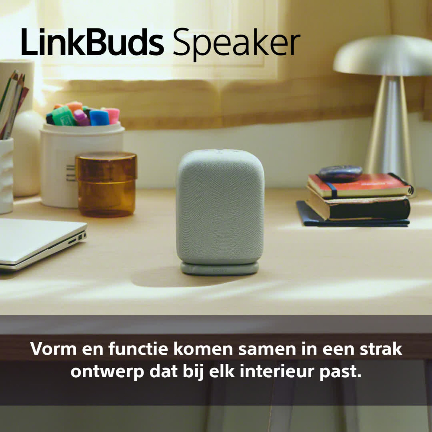 Een grijze luidspreker staat op een houten bureau met andere objecten, met tekst.