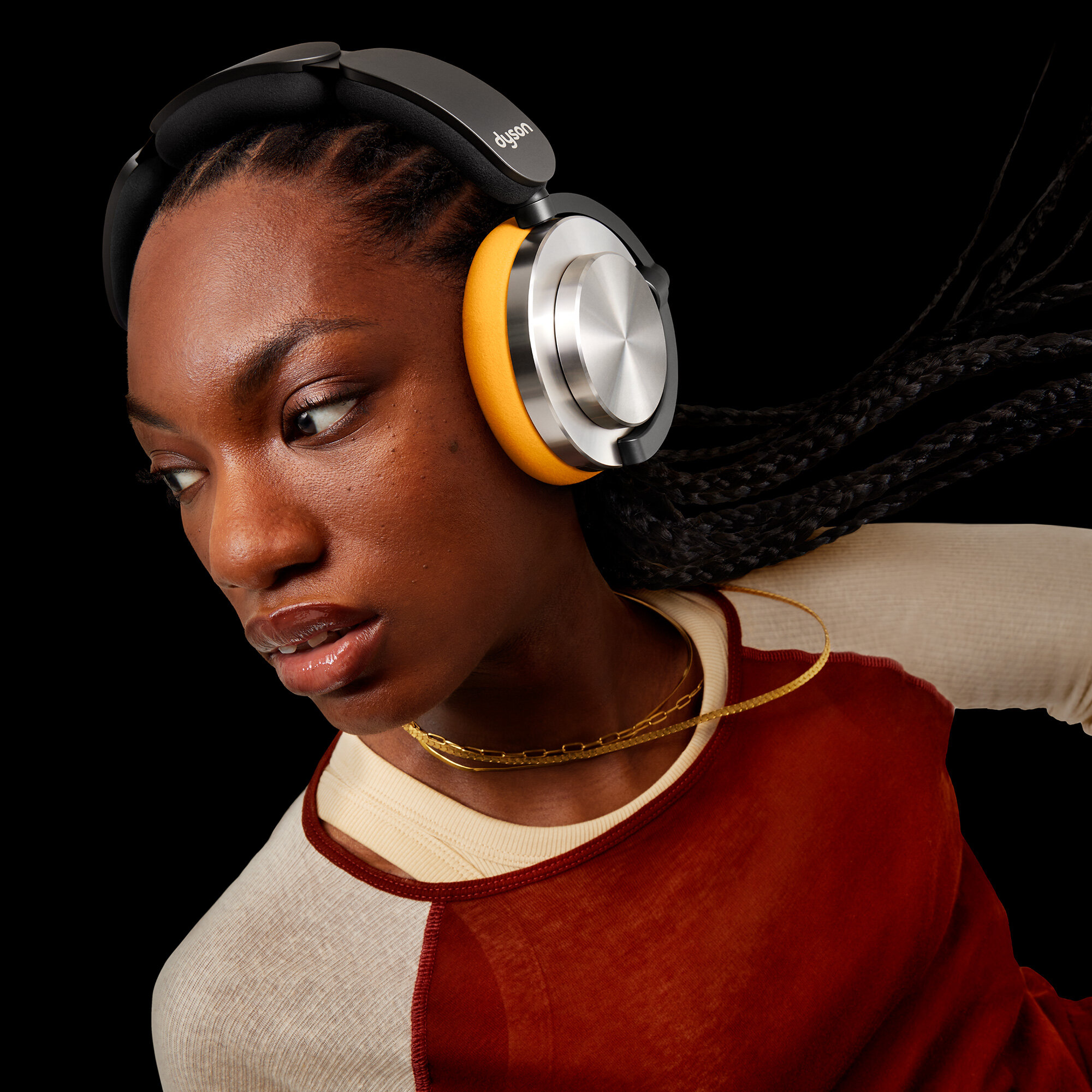 Kobieta w żółto-srebrnych słuchawkach, patrząca na bok, na czarnym tle.