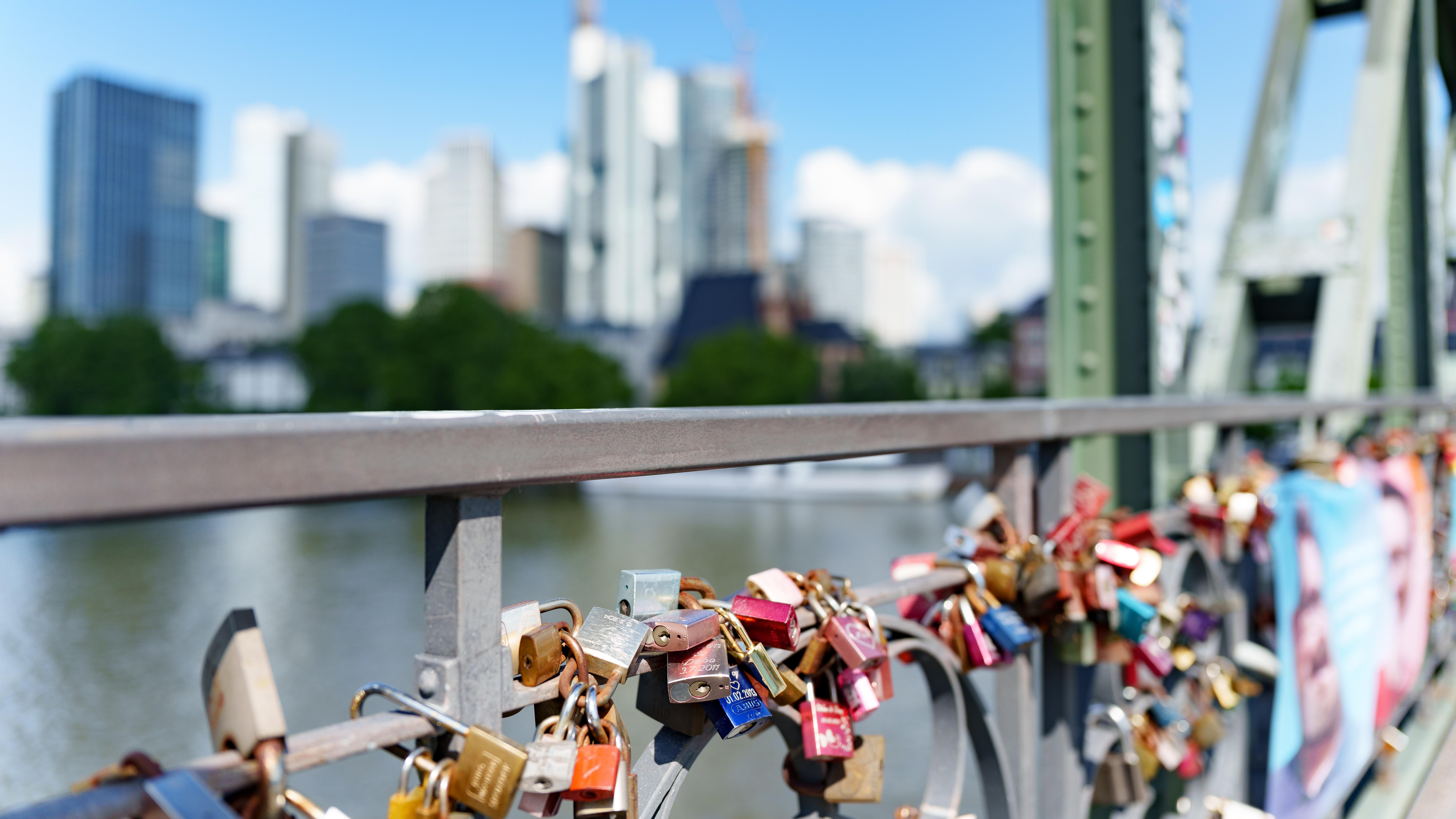 Brücke mit Schlössern am Geländer, Skyline im Hintergrund.