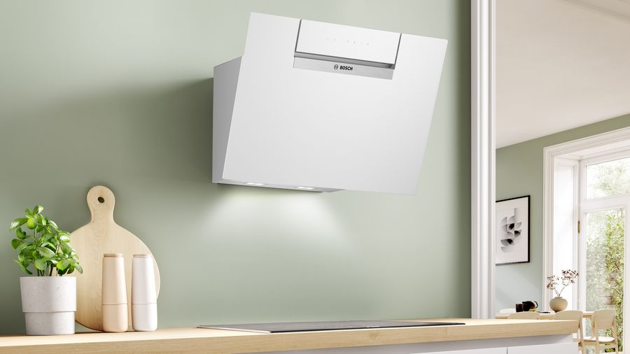 Campana extractora blanca en una pared verde claro. Una tabla de cortar de madera y utensilios de cocina.