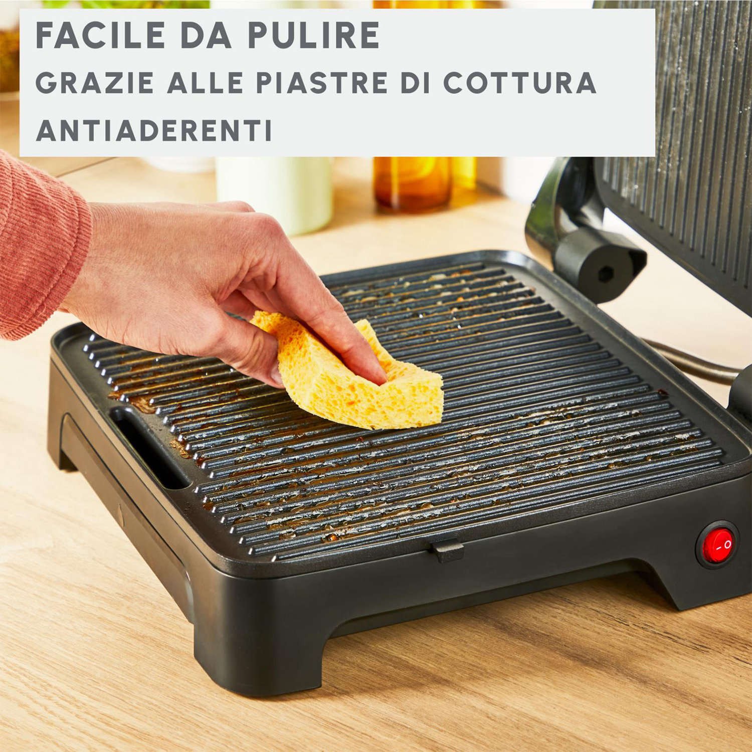 Persona che pulisce una griglia nera. Testo: Facile da pulire grazie alle piastre di cottura antiaderenti.