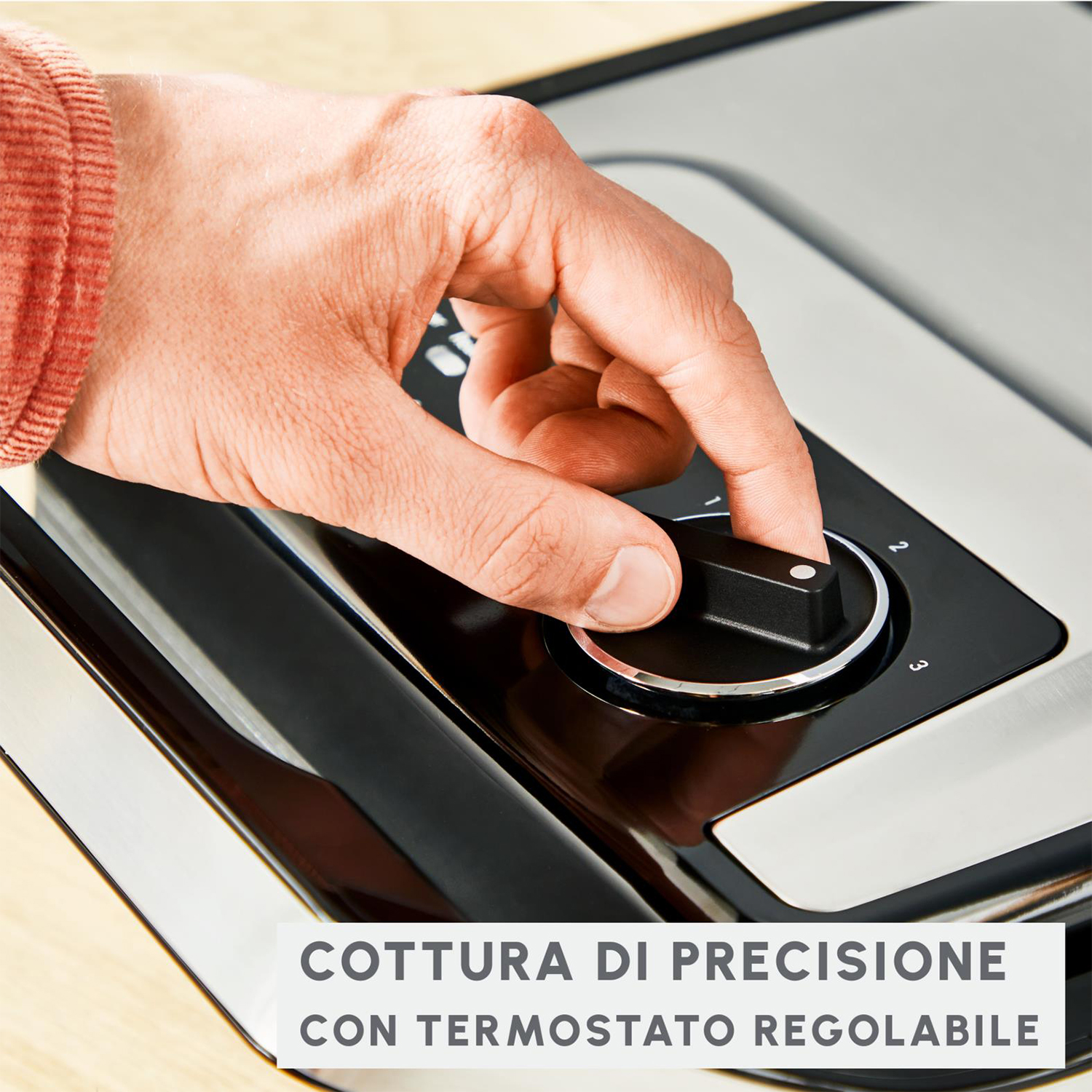 Una mano ruota un quadrante su un dispositivo nero e argento. Il testo in basso recita "COTTURA DI PRECISIONE".