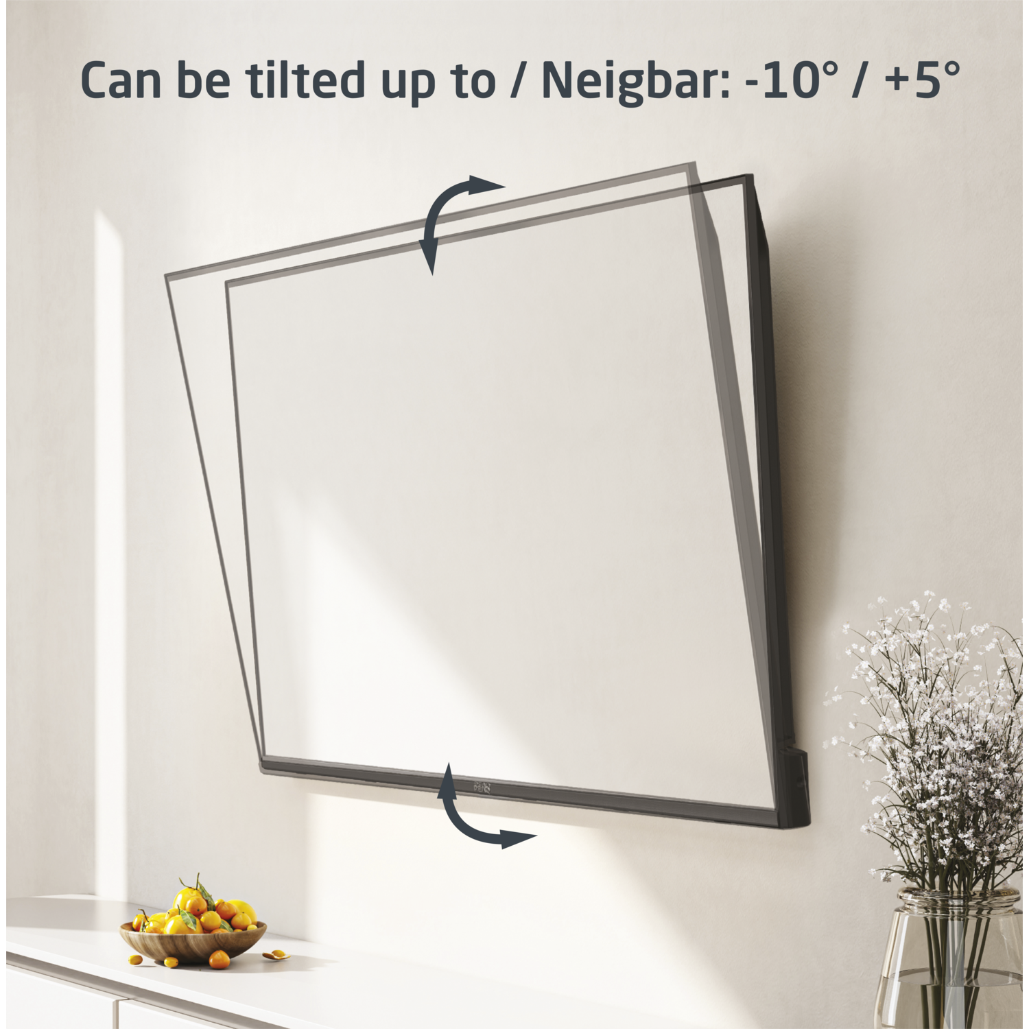 A TV screen mounted on a wall that can be tilted. A bowl of fruit and flowers are on the counter.