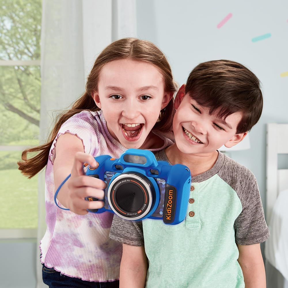 Dos niños sonrientes sostienen una cámara Kidizoom azul, en interiores.