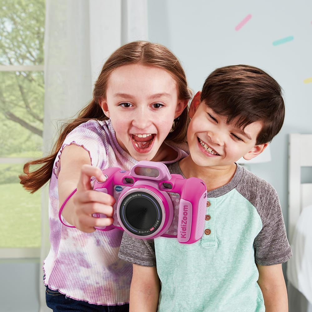 Dos niños sosteniendo una cámara Kidizoom rosa, sonriendo. La niña está tomando la foto, el niño sonríe.