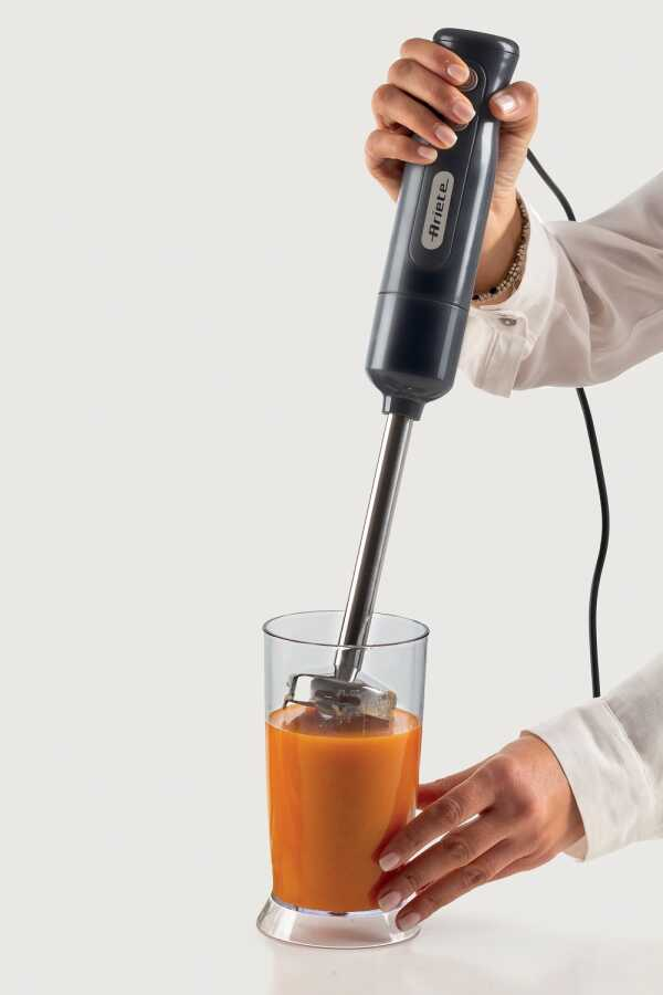 Bir el, bir bardakta turuncu sıvıyı karıştıran siyah bir el blenderi tutuyor.