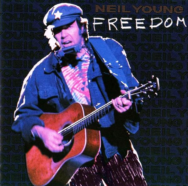 Neil Young auf der Bühne, spielt Gitarre, trägt Hut und Mundharmonika.