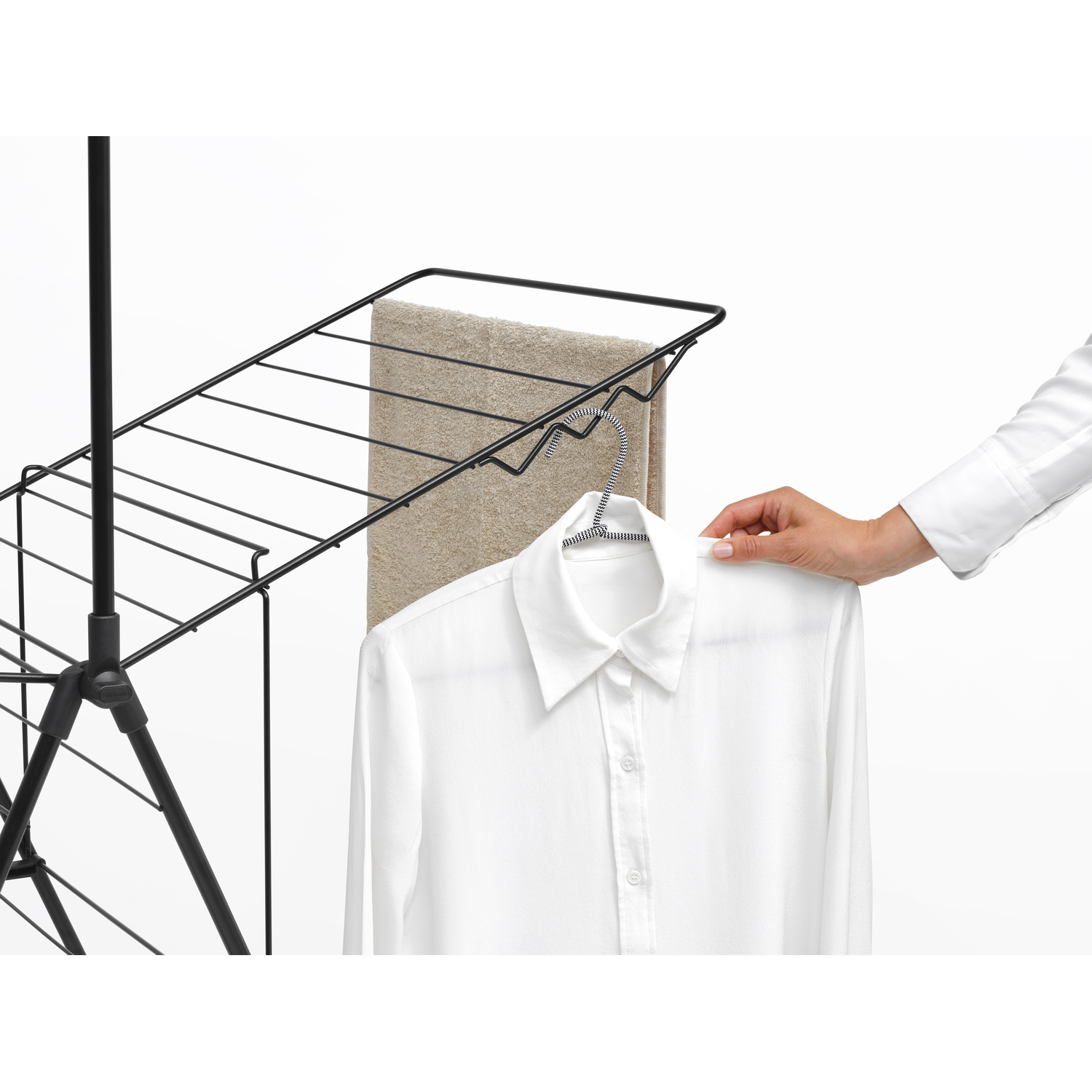 A drying rack with a towel and a white shirt hanging. A hand is reaching to the shirt.