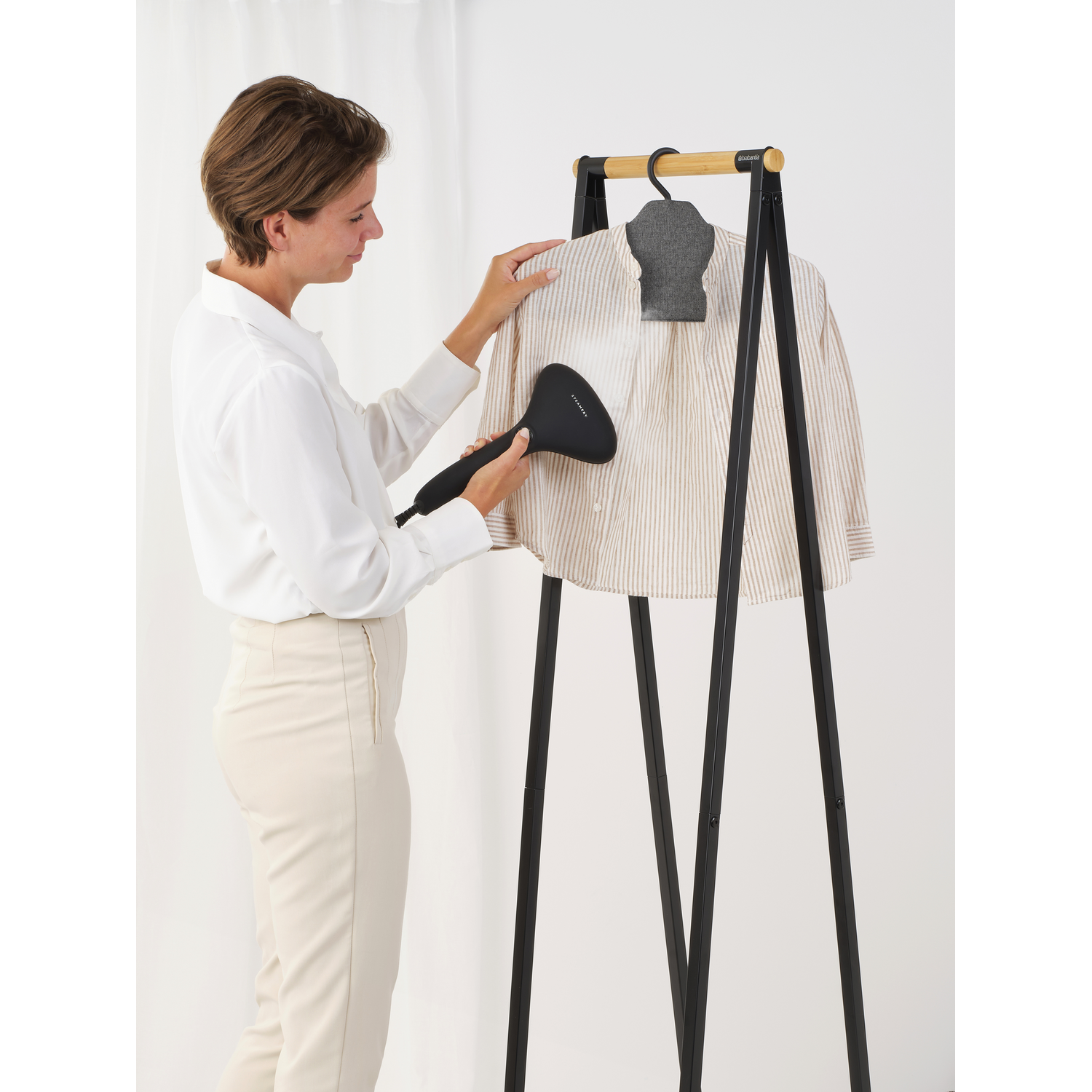 Vrouw die een gestreept overhemd strijkt op een kledingrek met een zwart en houten frame.