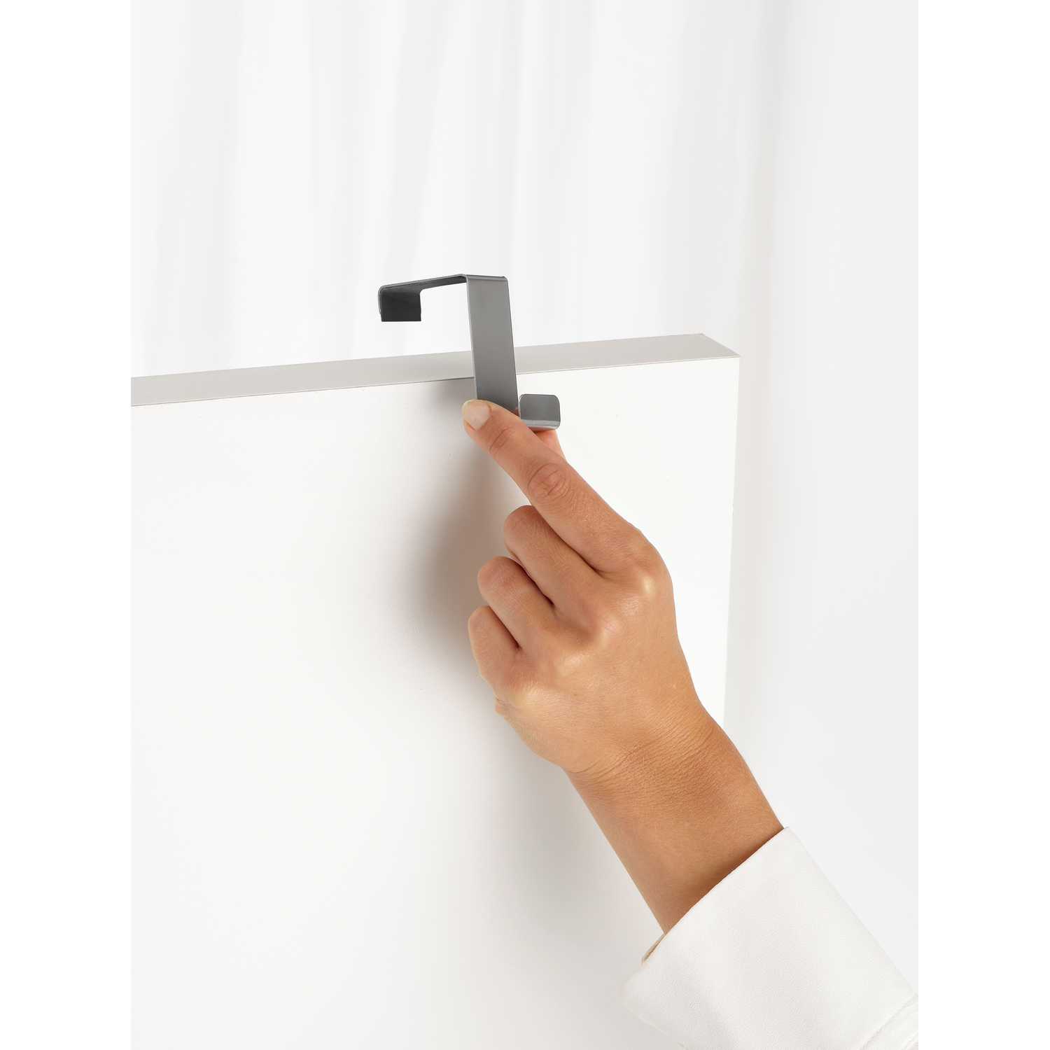 Main plaçant un crochet gris sur une porte blanche. Éclairage doux.