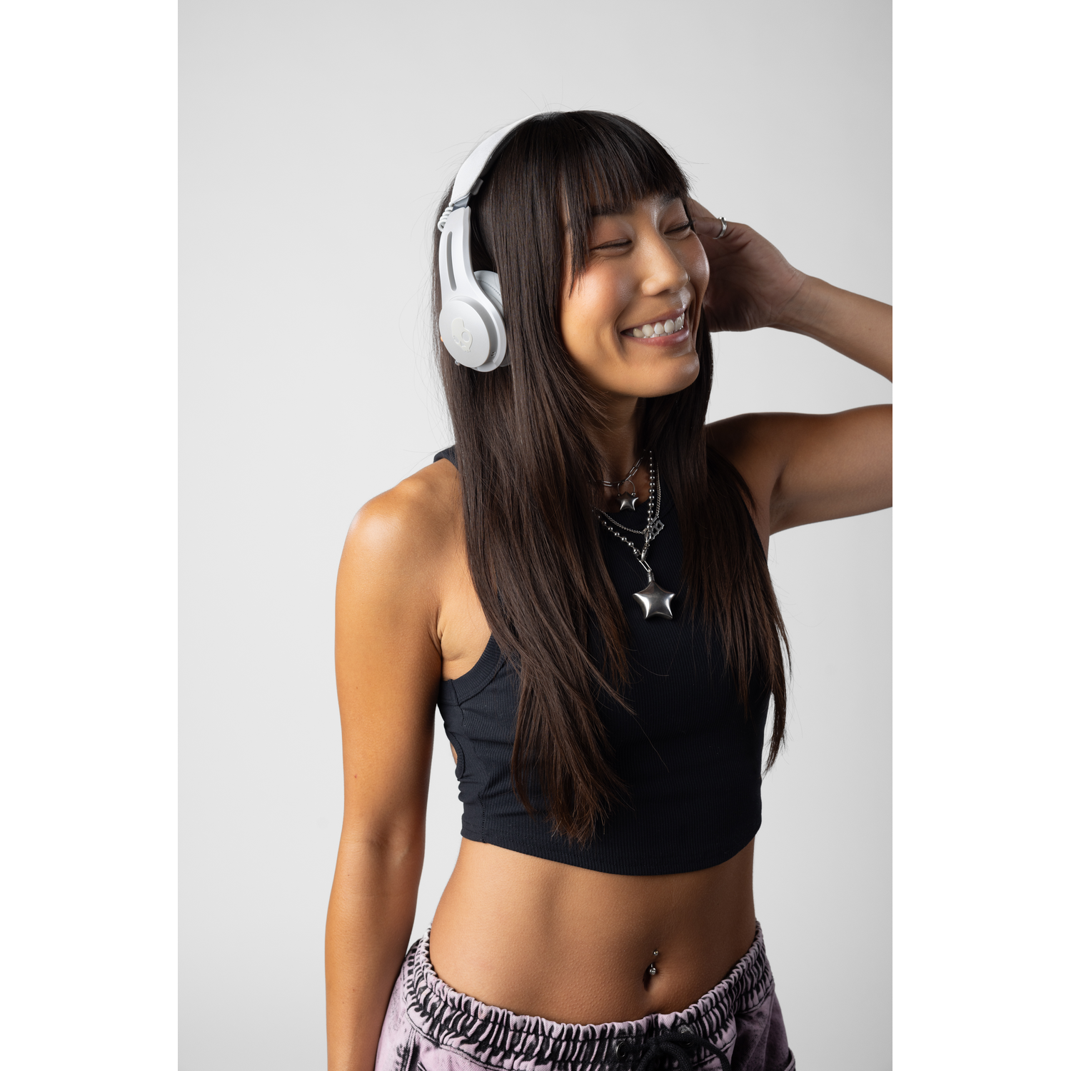 A woman smiles wearing white headphones, black top, and pink pants.