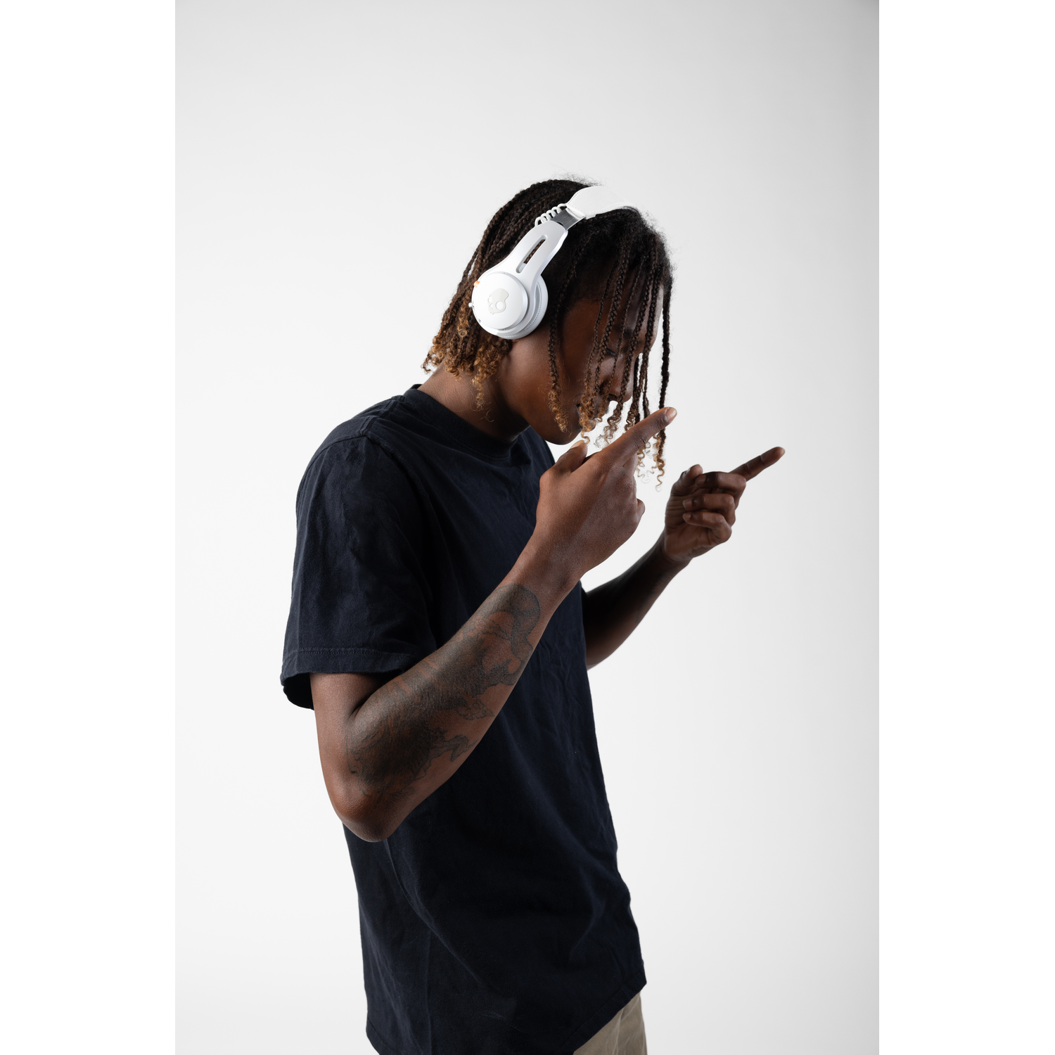 A man with dreadlocks wearing white headphones points fingers. White background.