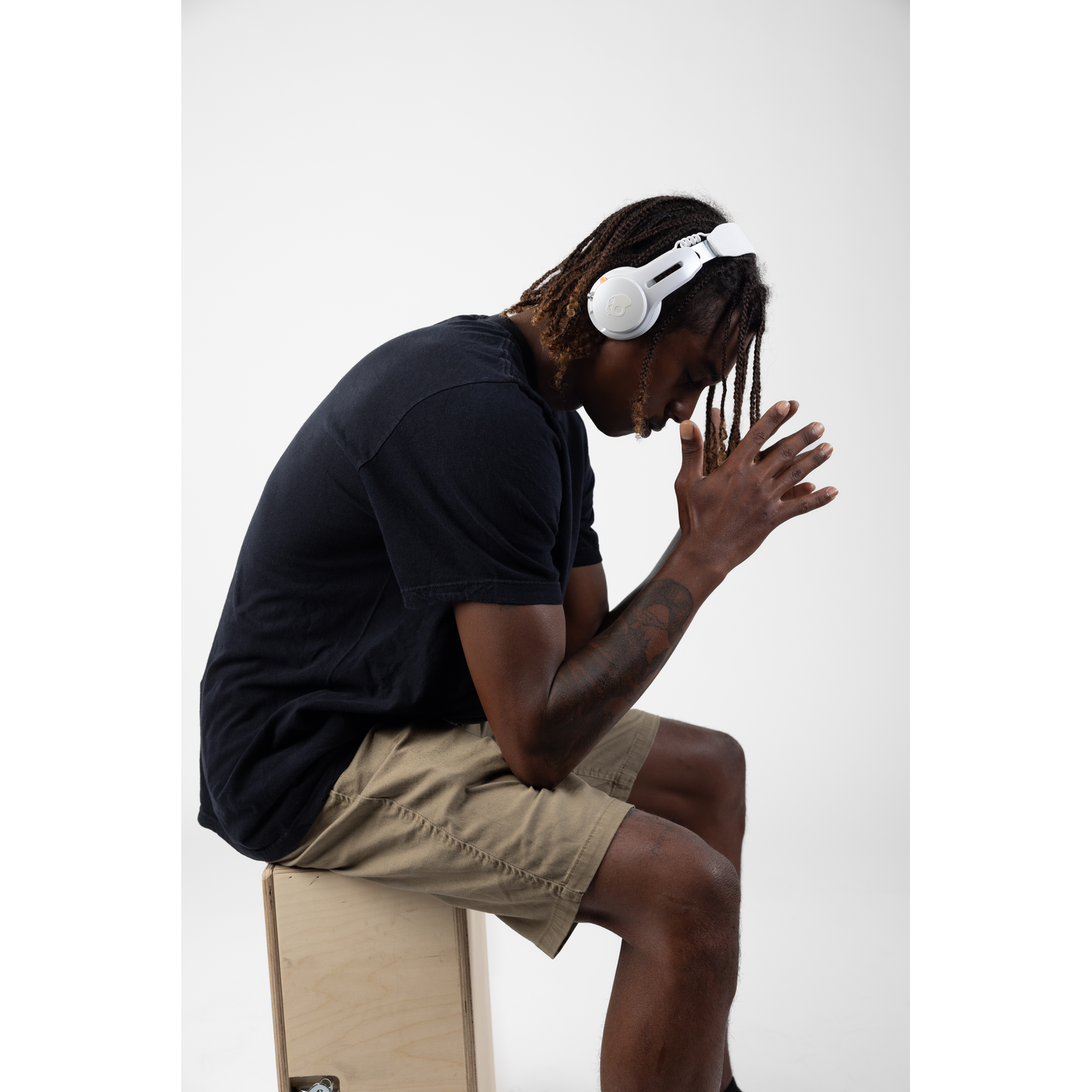 A person with braids wearing white headphones, sitting and looking down.
