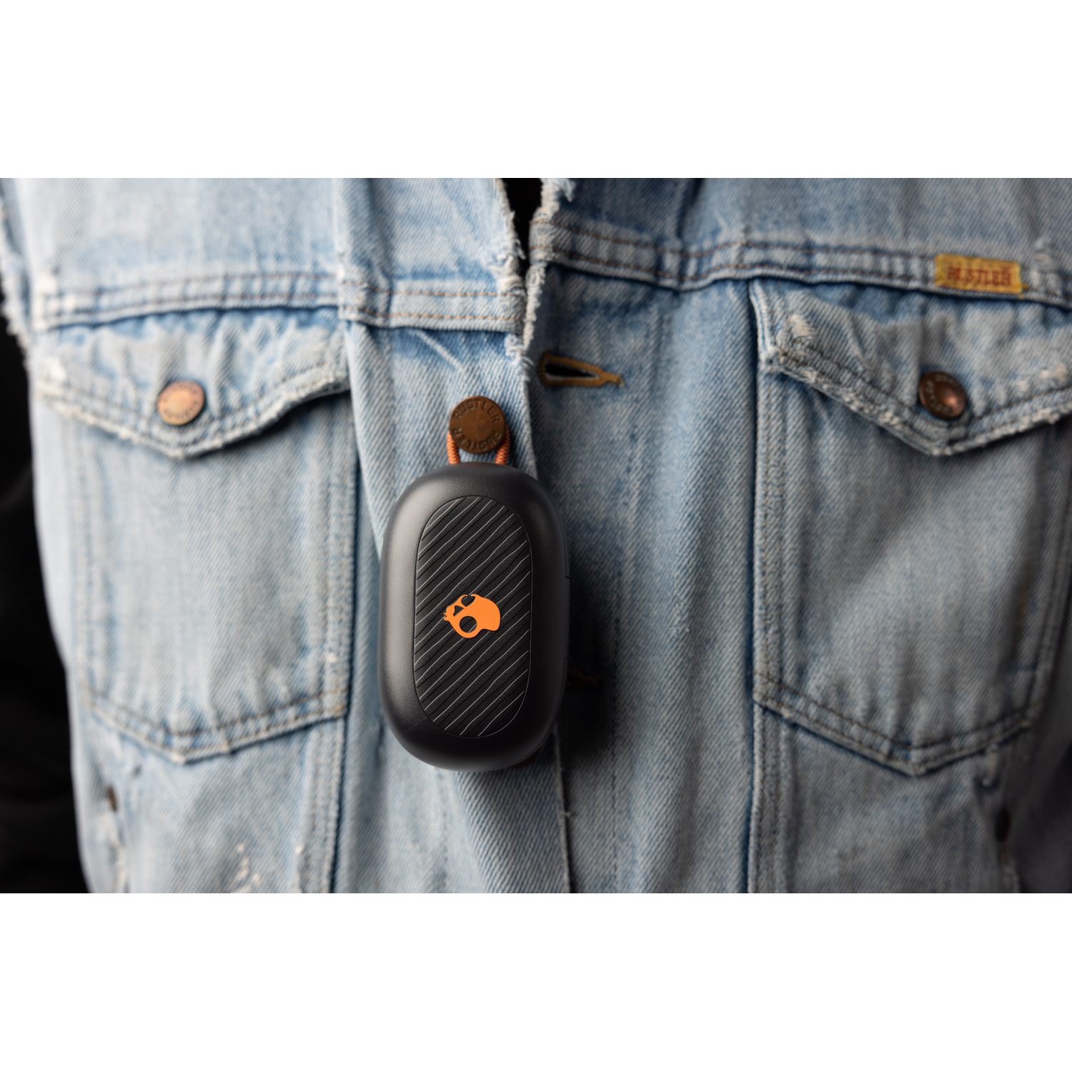 A black Skullcandy wireless earbud case, attached to a denim jacket.
