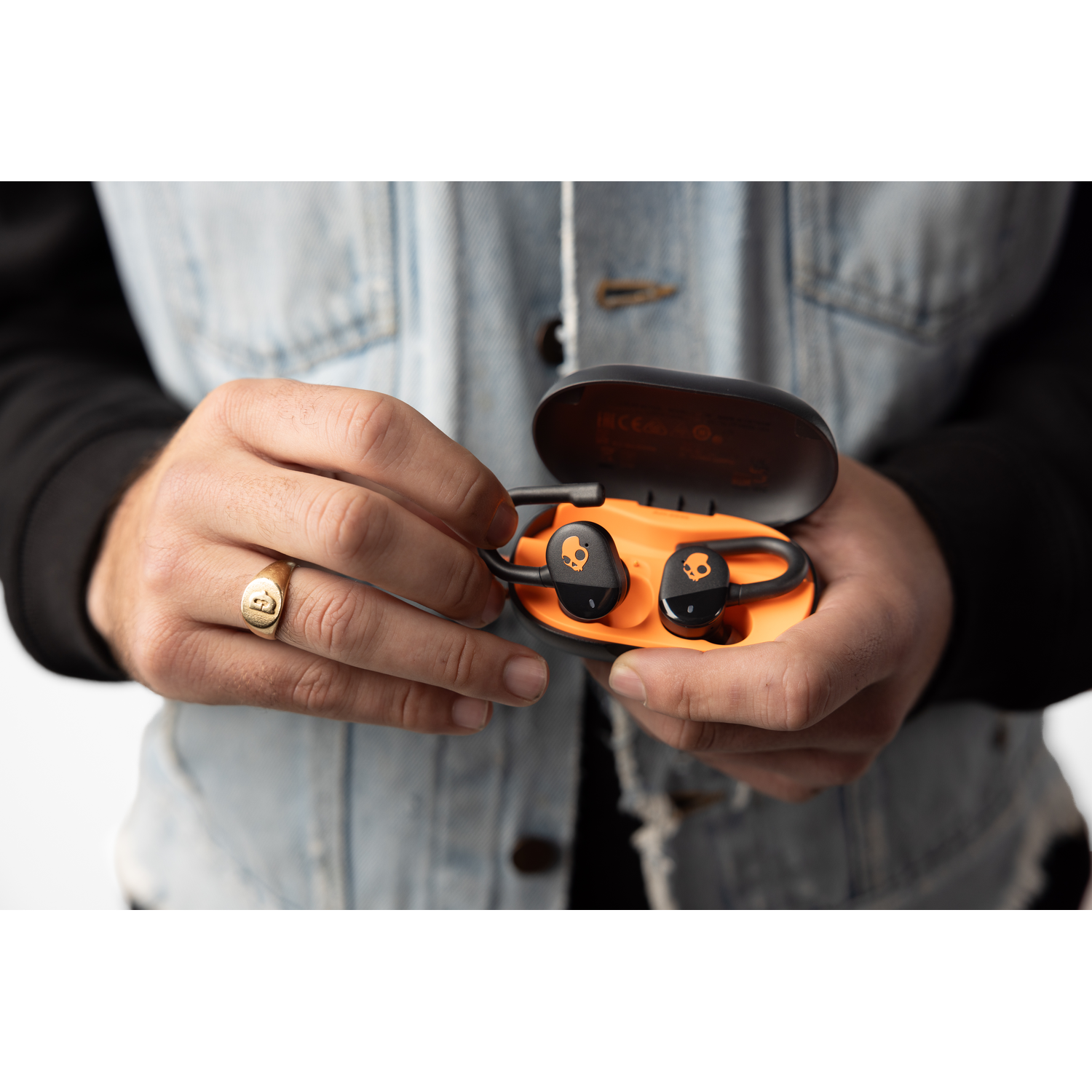 A person holding an open orange case with black skull-shaped earbuds inside.