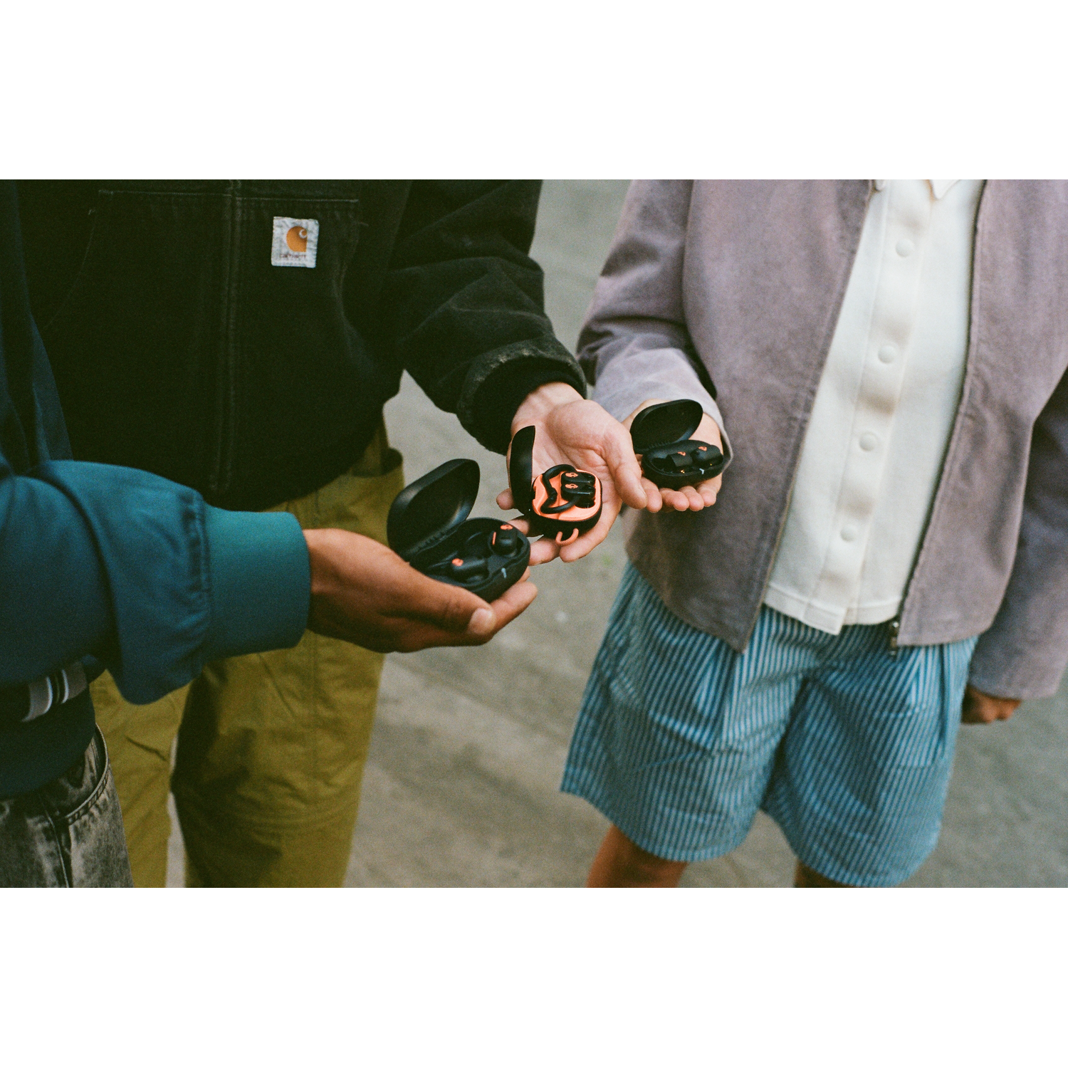 Three people holding black earbud cases open, on a light background.