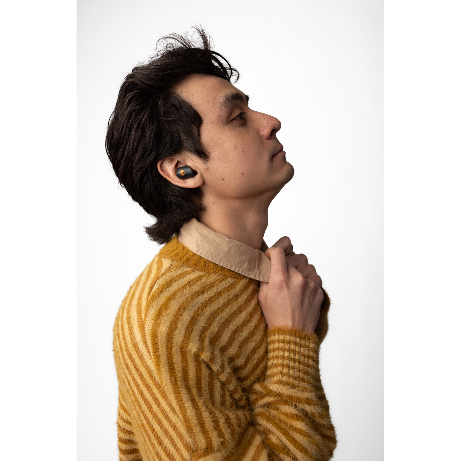 Man wearing earbuds looking up. He is in a yellow sweater, with a white background.