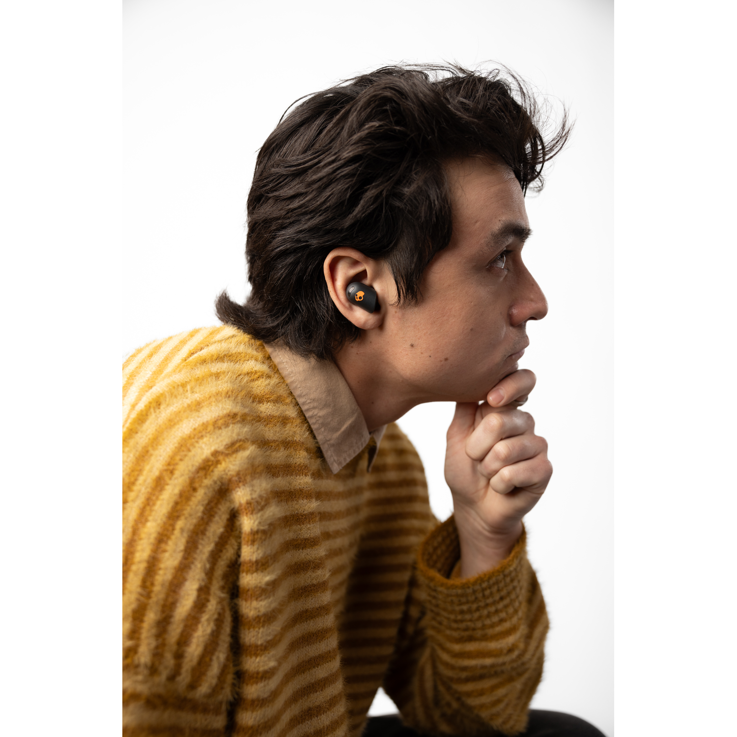 A man wearing yellow sweater with black earbuds in his ears, looking to the side, white background.