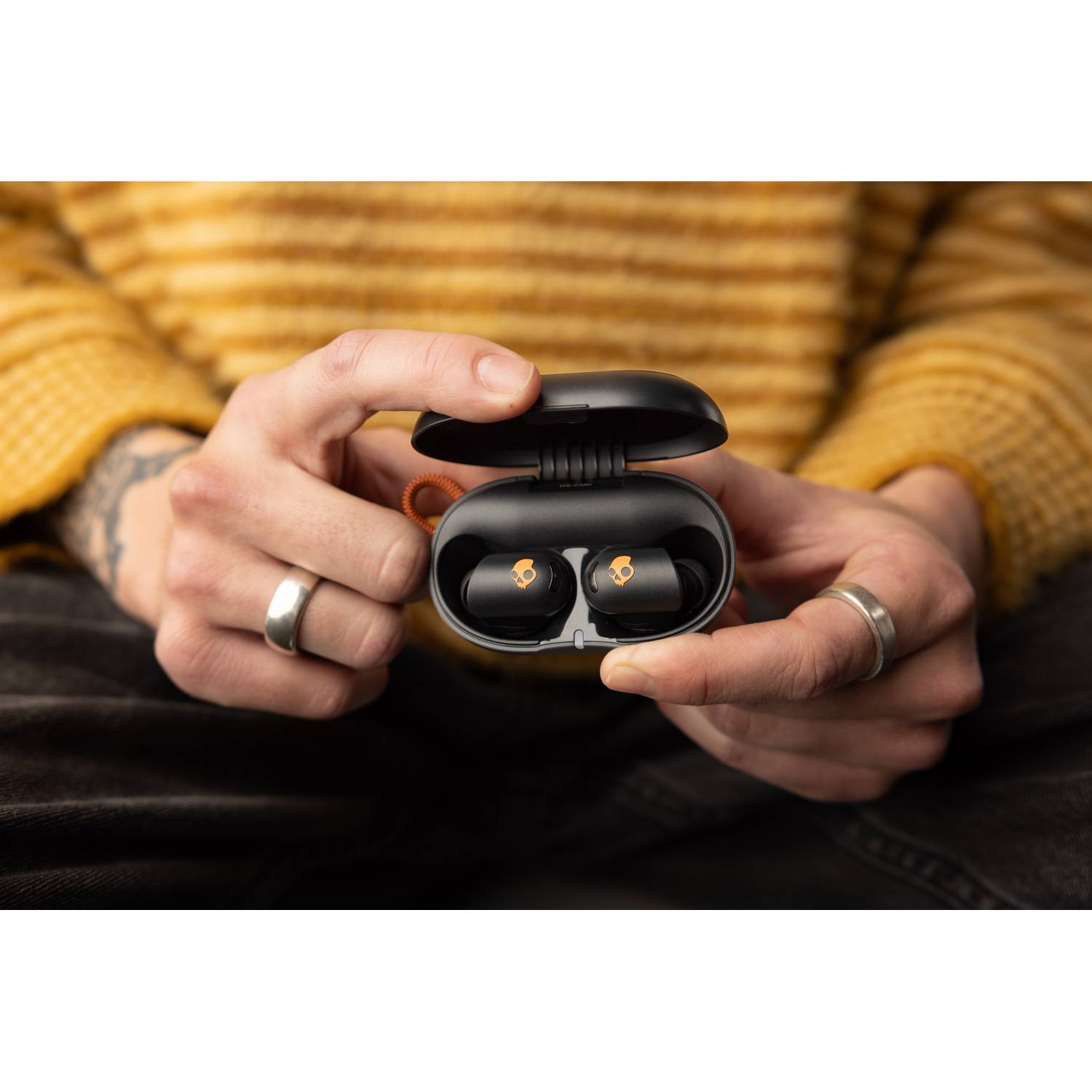 Two hands holding a black earbud case with earbuds inside.