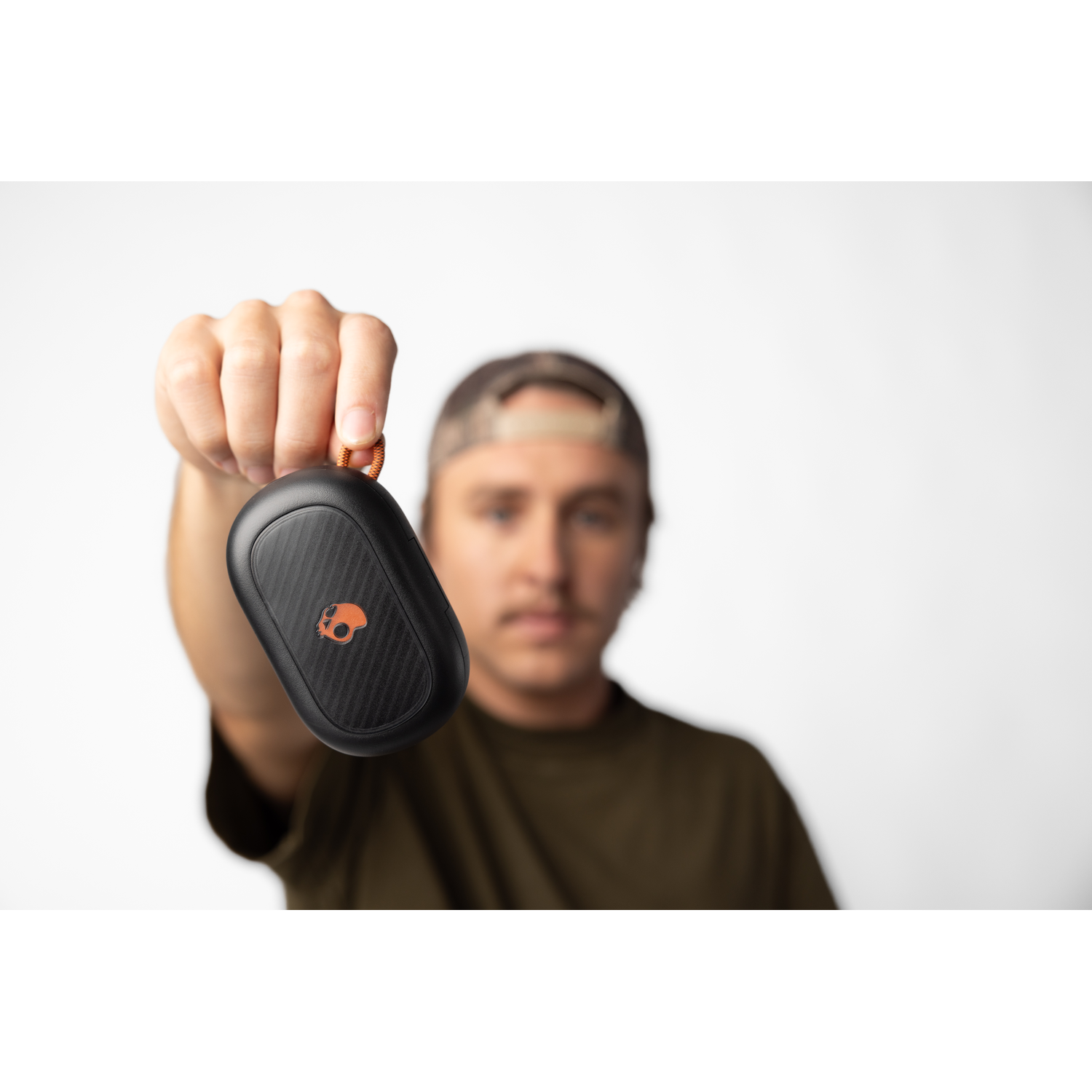 Man holding a black Skullcandy speaker with orange logo, against a white background.