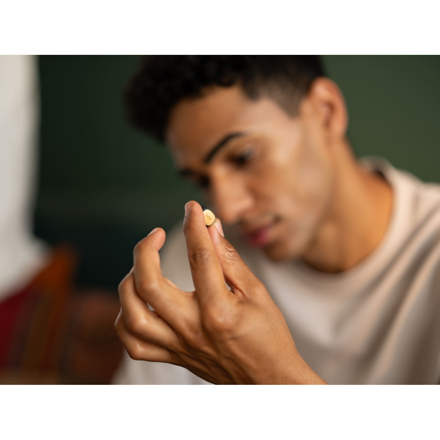 Man holding a small round pill with a yellow face. Blurred background.