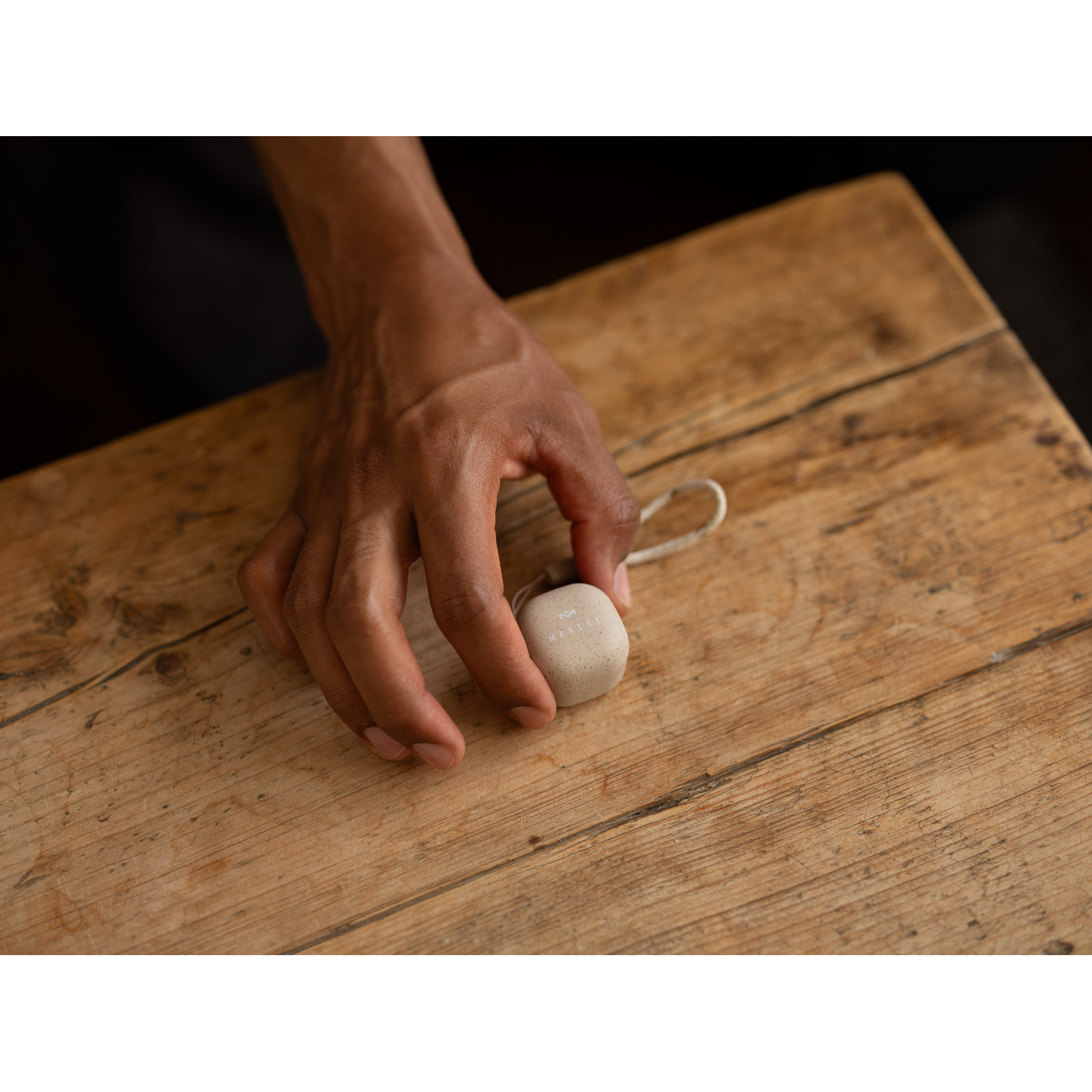 A hand holding a small, neutral-colored, rounded object on a wooden surface.