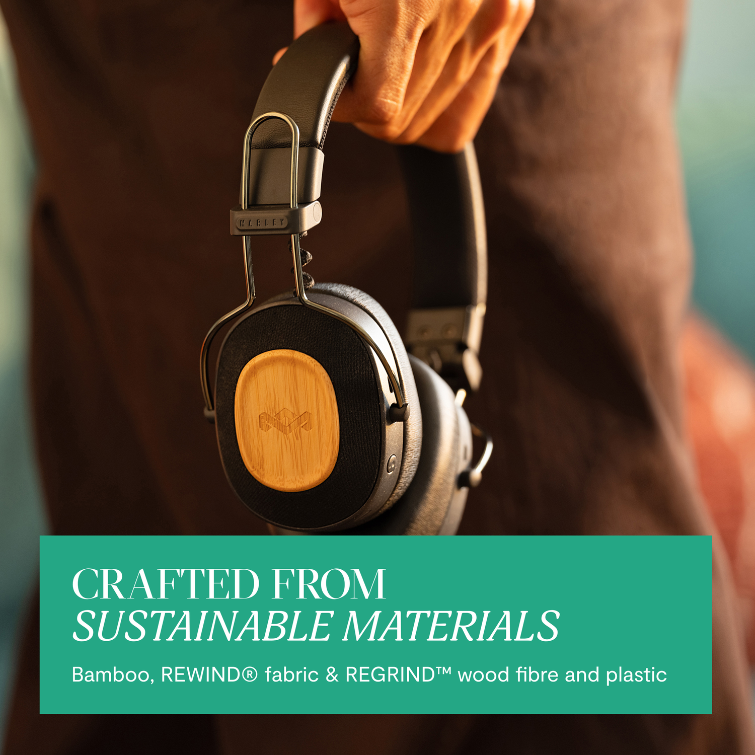 A person holding black headphones with wood accents, text says 'Crafted From Sustainable Materials'.