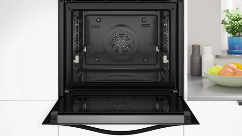Interior de horno abierto con ventilador y rejillas. Gabinetes blancos y encimera con plantas.