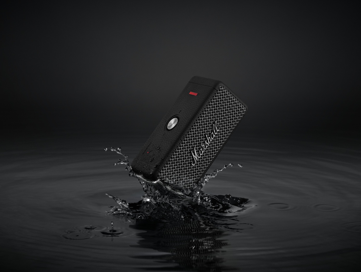 Un altavoz negro salpica agua. El altavoz tiene una rejilla de malla plateada y una luz roja visible.