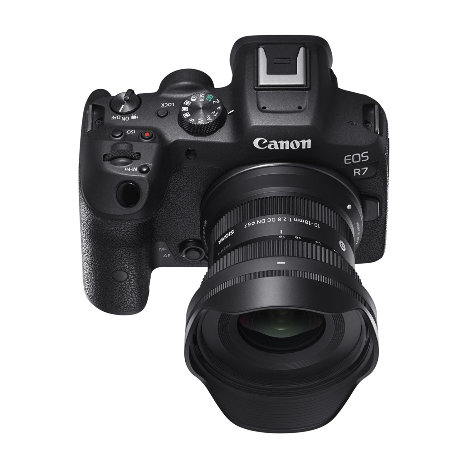 Una fotocamera Canon EOS R7 nera con un obiettivo Sigma. La fotocamera è su una superficie bianca.