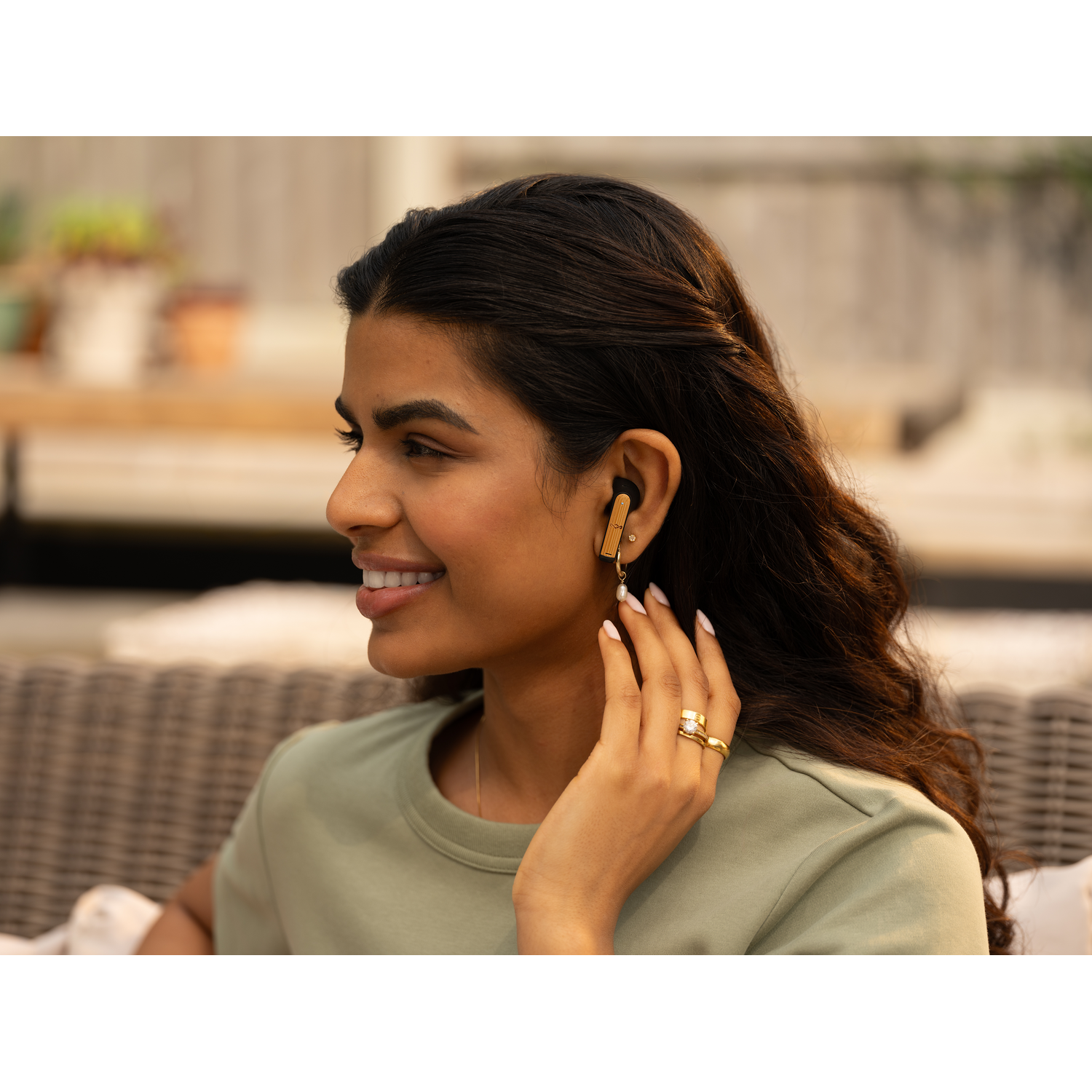 Woman smiling, wearing an earbud, with a ring, outdoor setting.