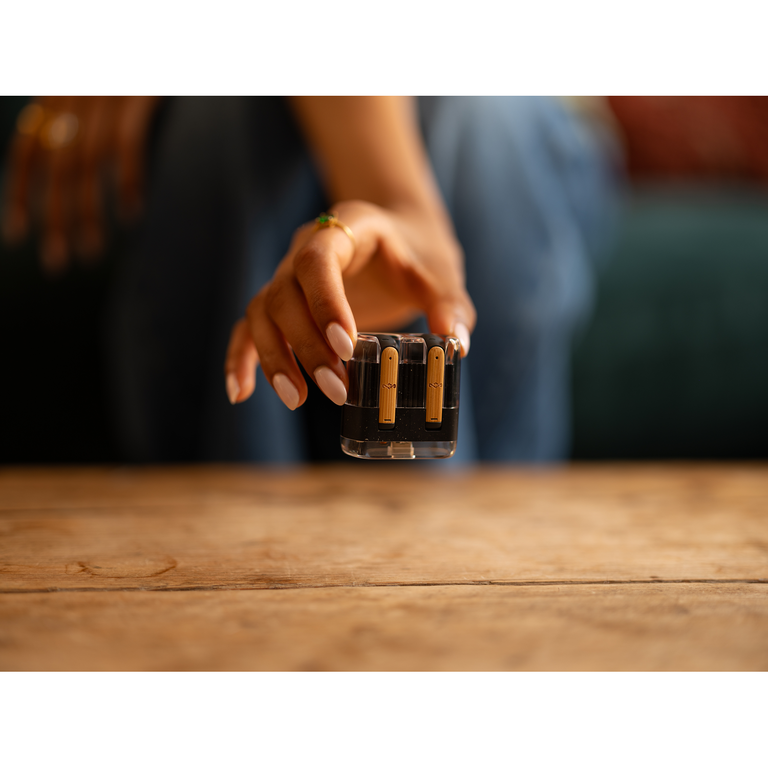 A hand reaching towards a clear plastic adapter with gold prongs, placed on a wooden surface.