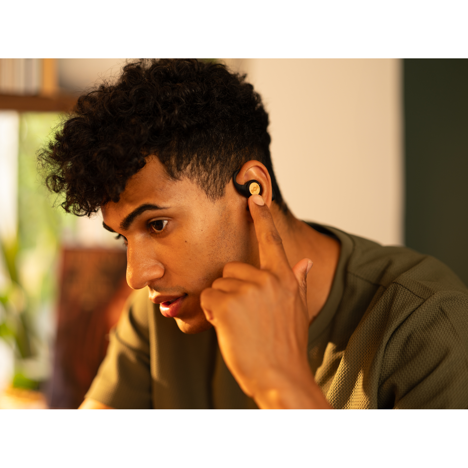 A man wearing a green shirt and using gold earbuds in his ear.