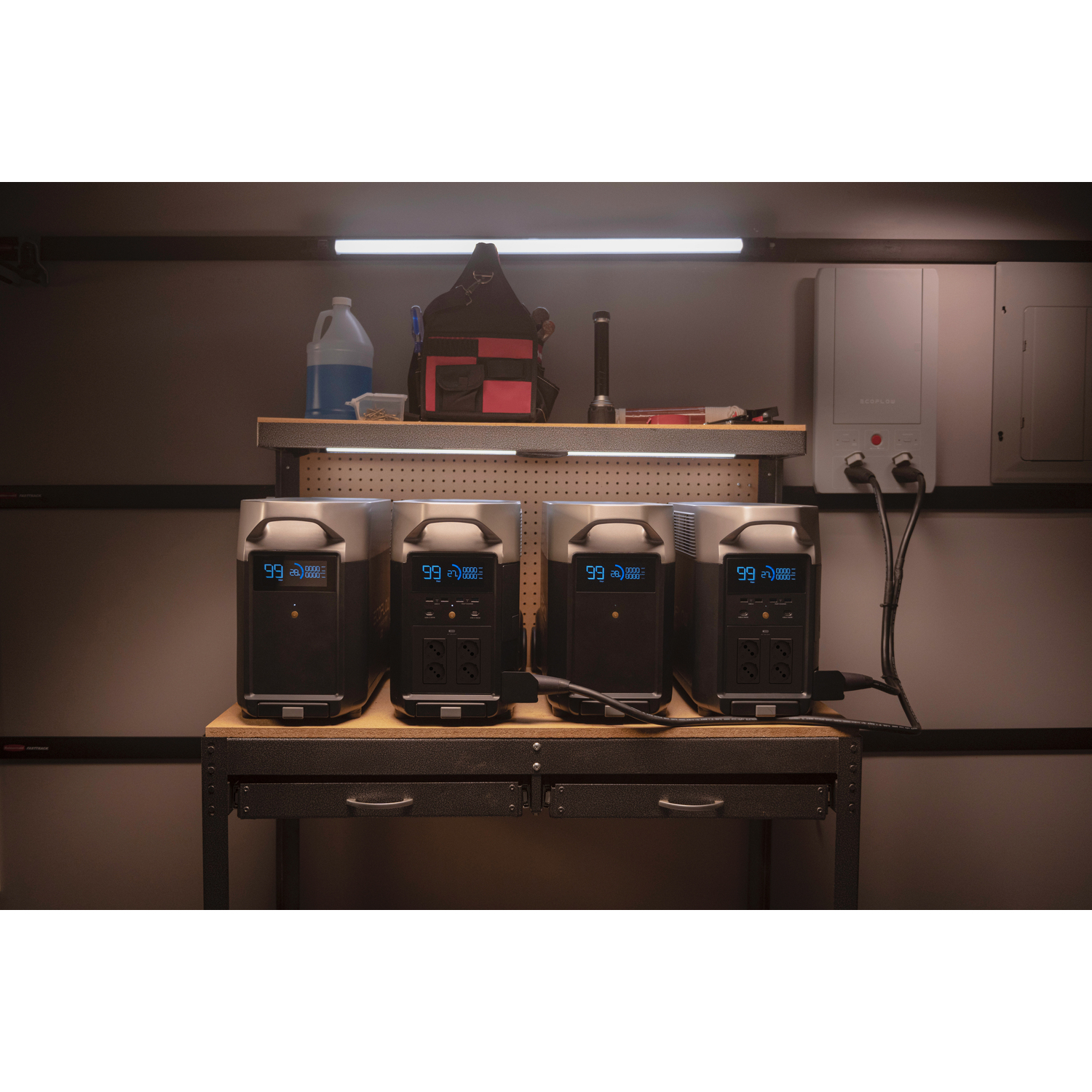 Quatre centrales électriques noires avec écrans numériques, disposées sur une étagère en bois dans un cadre de garage.
