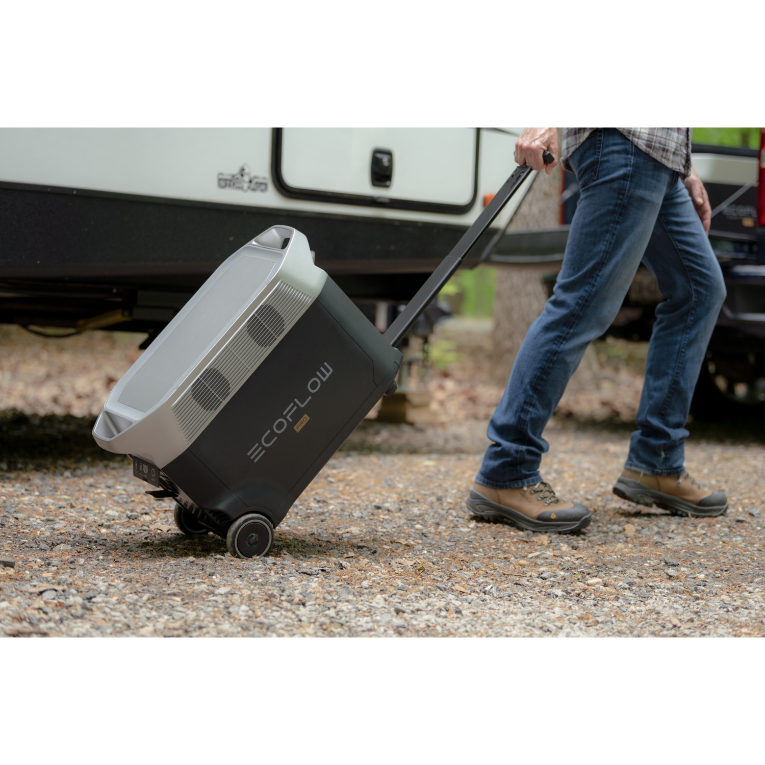 Une personne tirant une centrale électrique portable ECOFLOW PRO noire et argentée sur roues dans un cadre forestier.