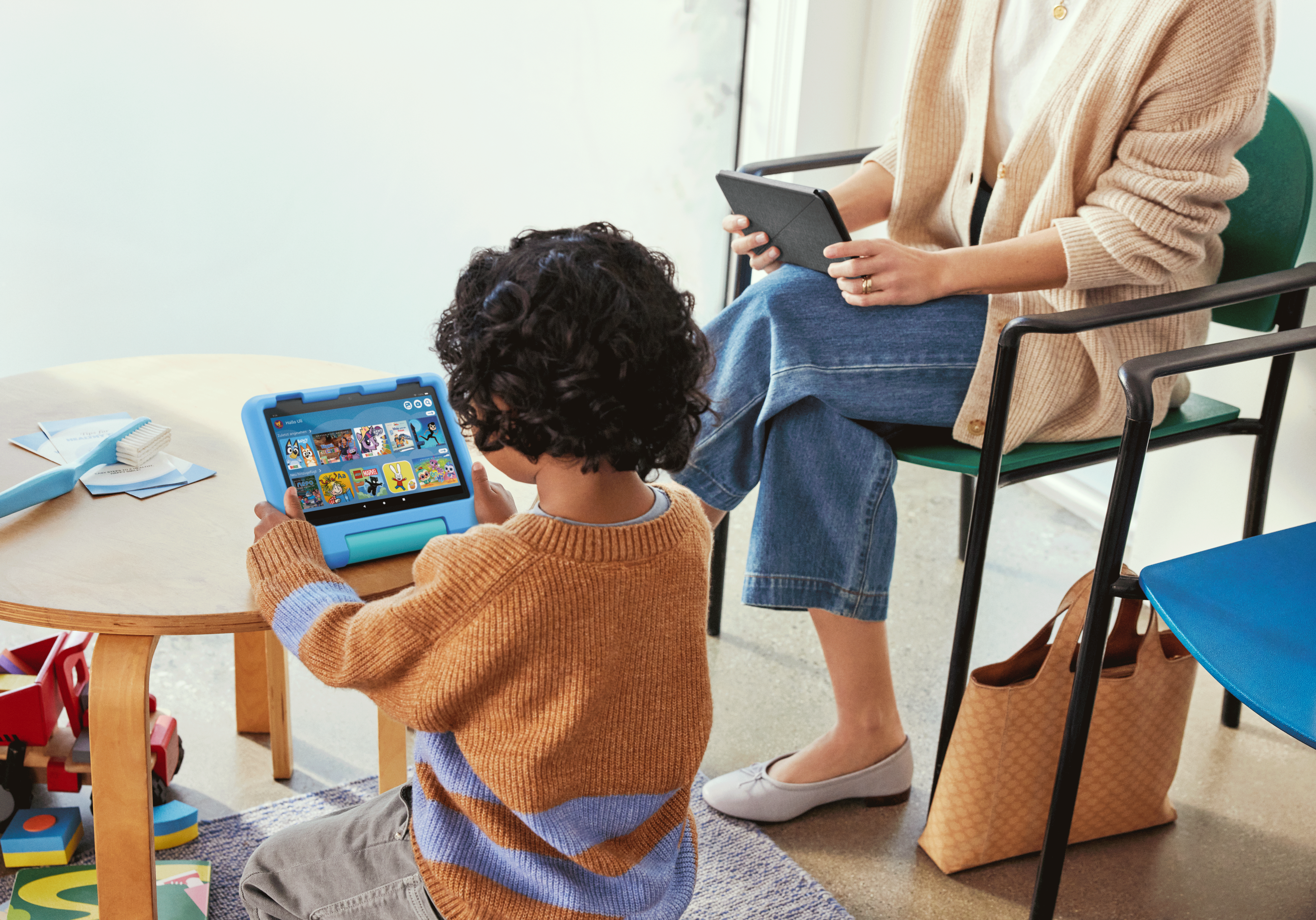 Ein Kind benutzt ein Tablet, und ein Erwachsener hält eins. Beide sind in einem Wohnzimmer.
