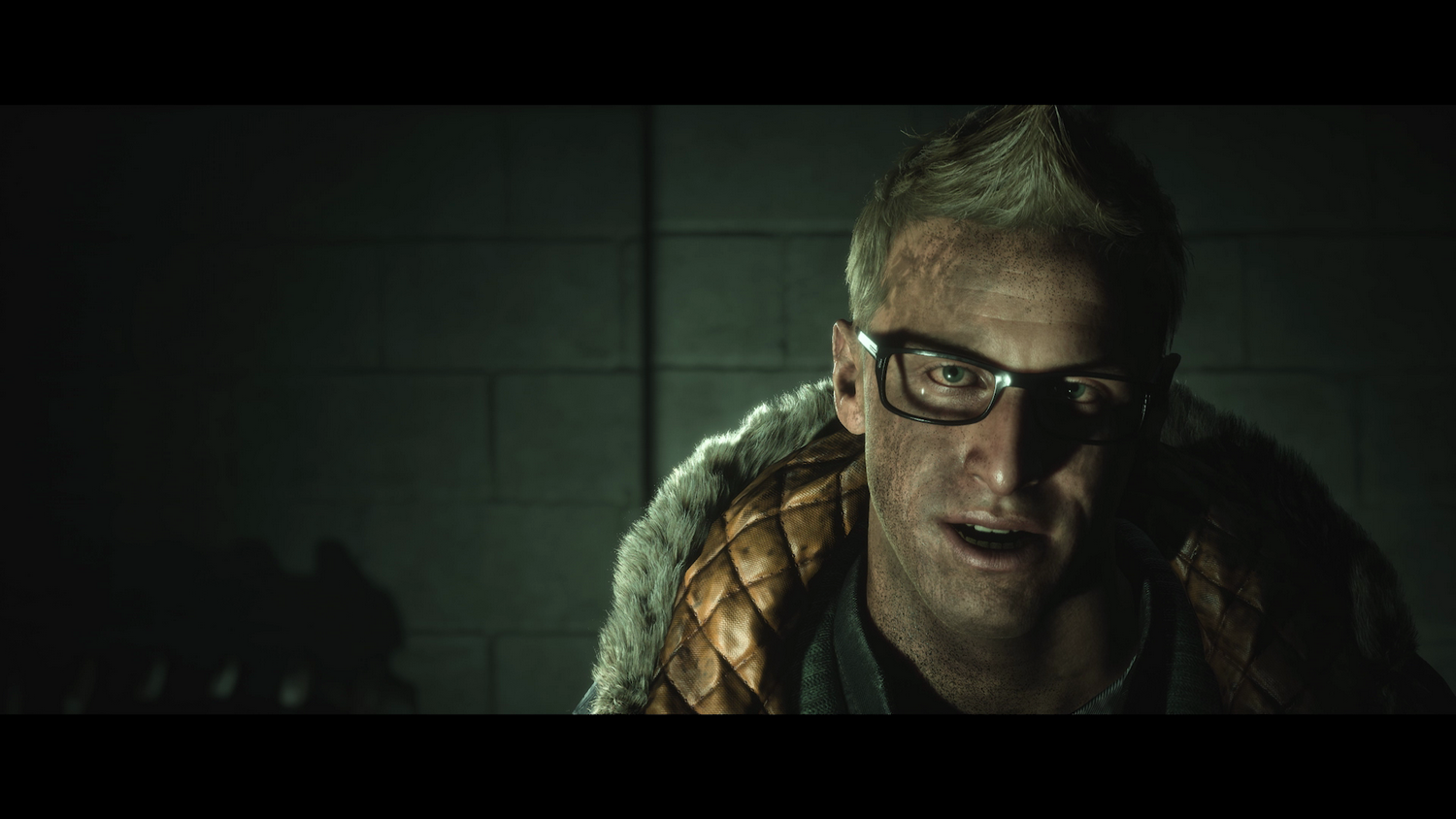 Un hombre con gafas en un ambiente oscuro. Mira a la cámara y tiene una chaqueta de piel.