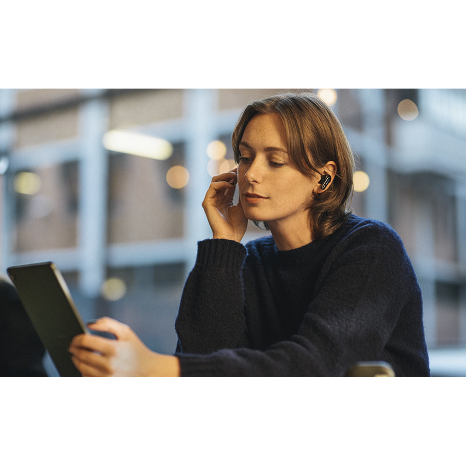 Woman in a cafe using a tablet and wearing black wireless earbuds.