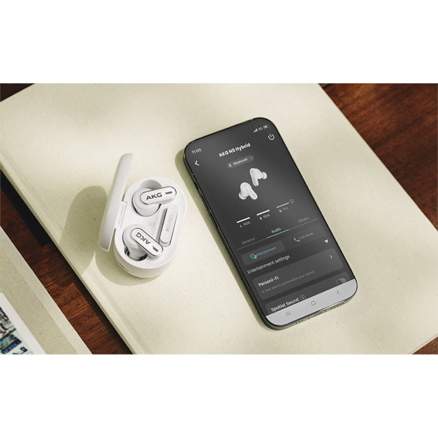 White AKG earbuds with case next to a phone screen displaying the app interface.