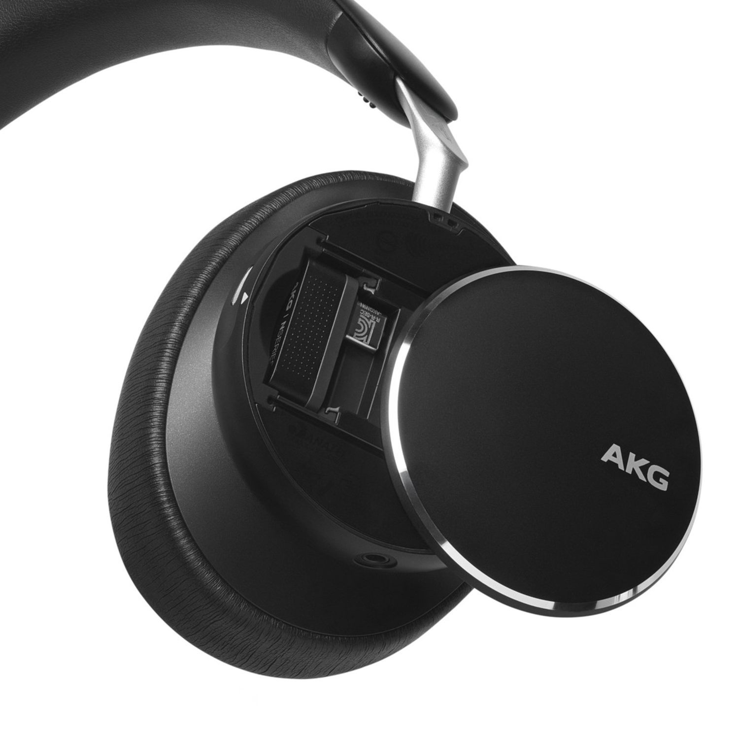 Black AKG headphones, open, showing internal components and a battery. Black background.