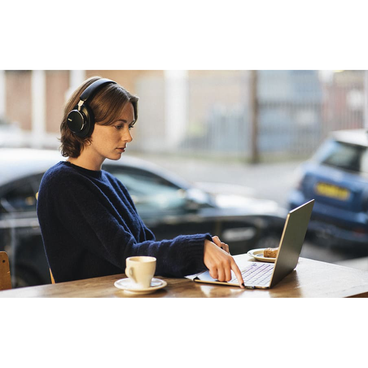 A woman wearing headphones working on a laptop in a cafe.