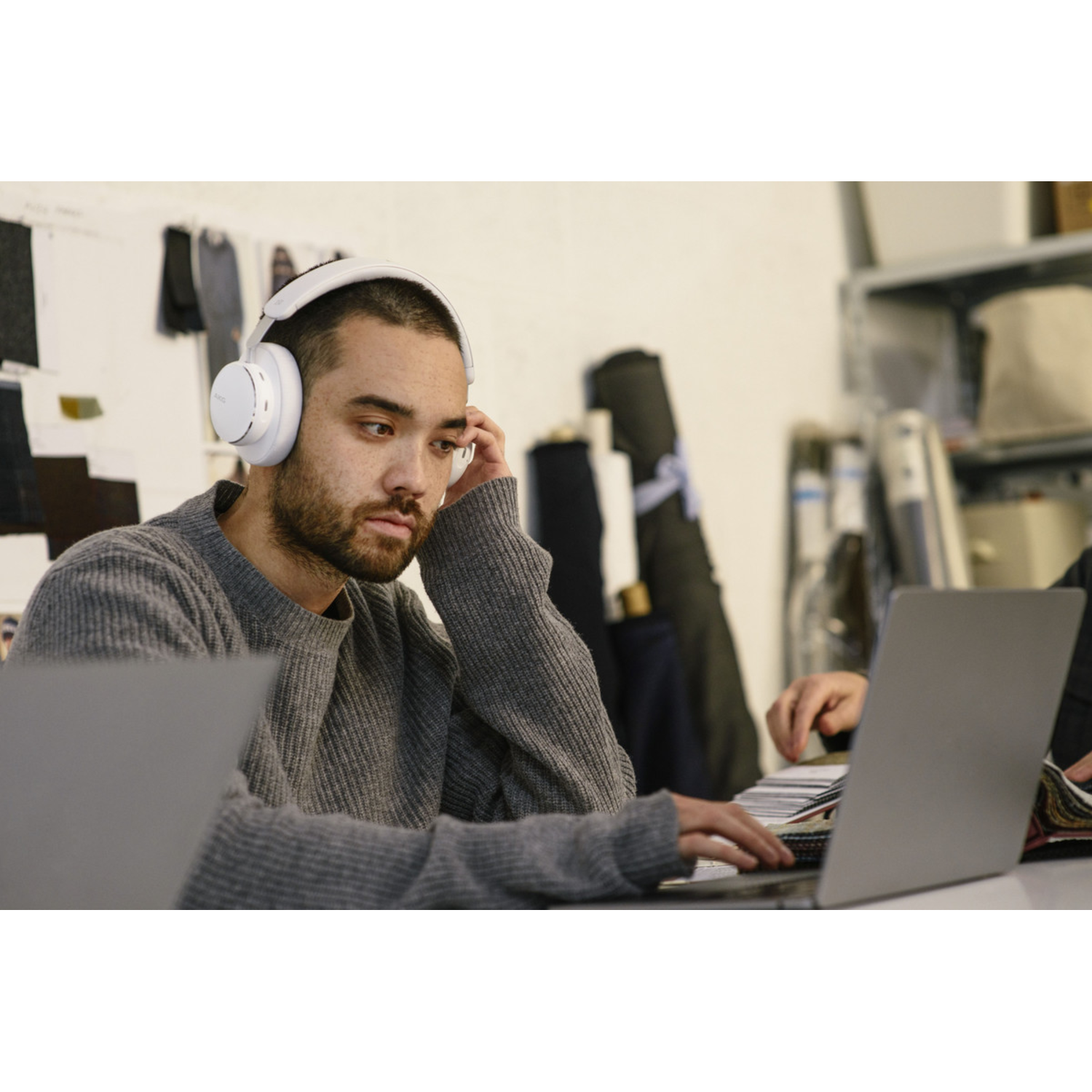 Een man met een witte koptelefoon, geconcentreerd op een laptop. Een andere persoon is zichtbaar.